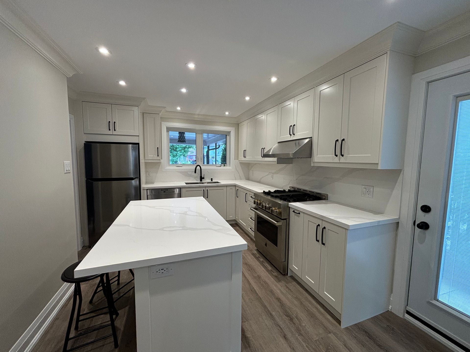 White kitchen with stainless steel appliances, marble countertops, and a center island.
