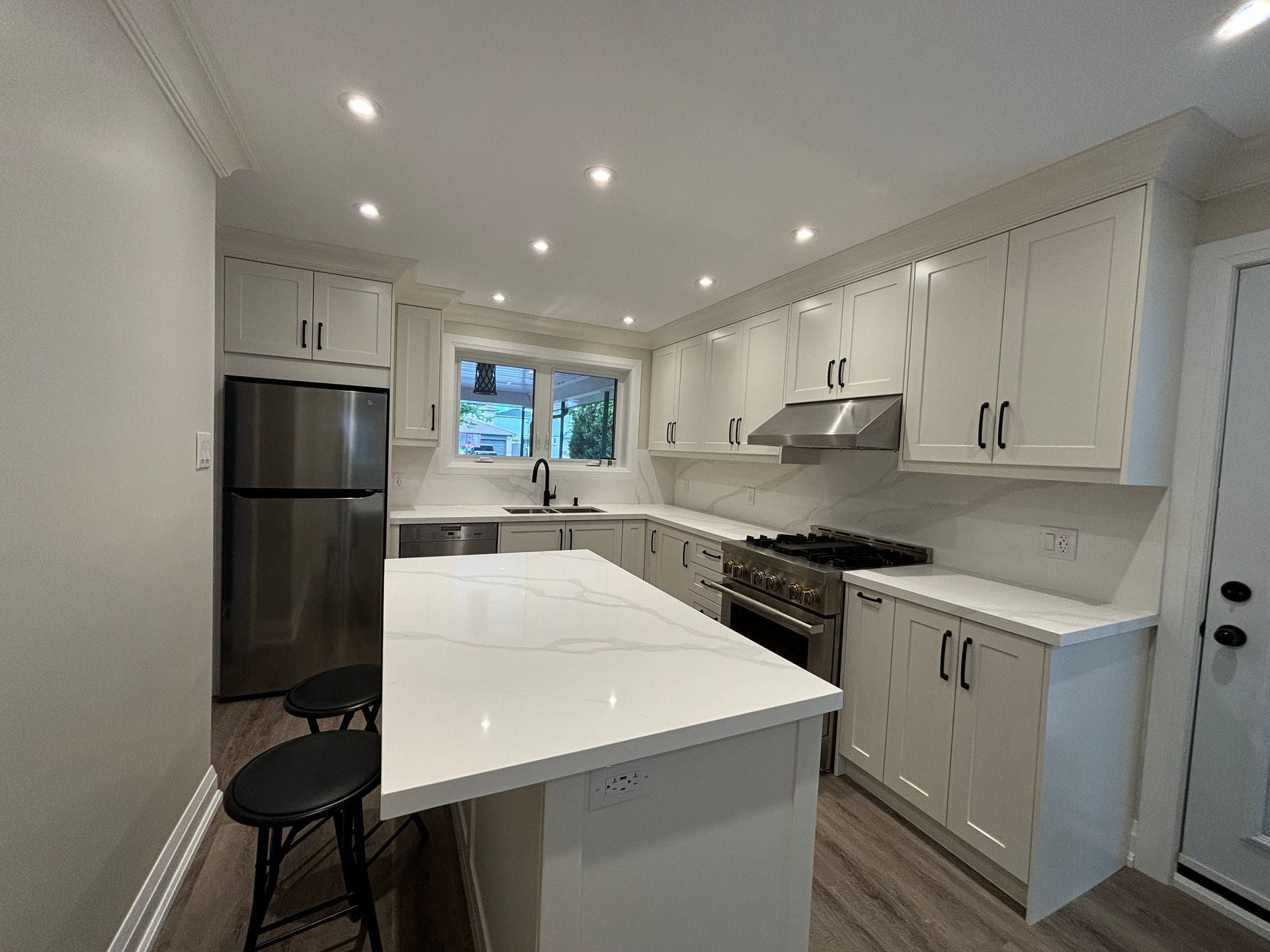 Modern white kitchen with island, stainless steel appliances, and black hardware.
