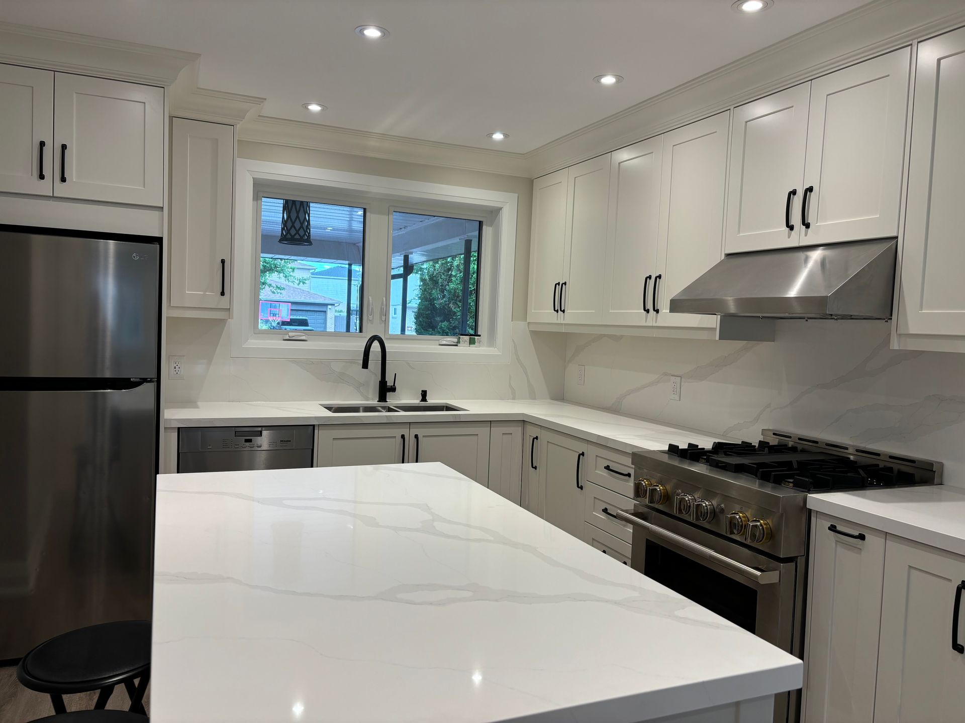 Modern white kitchen with stainless steel appliances, marble countertops, and black hardware.