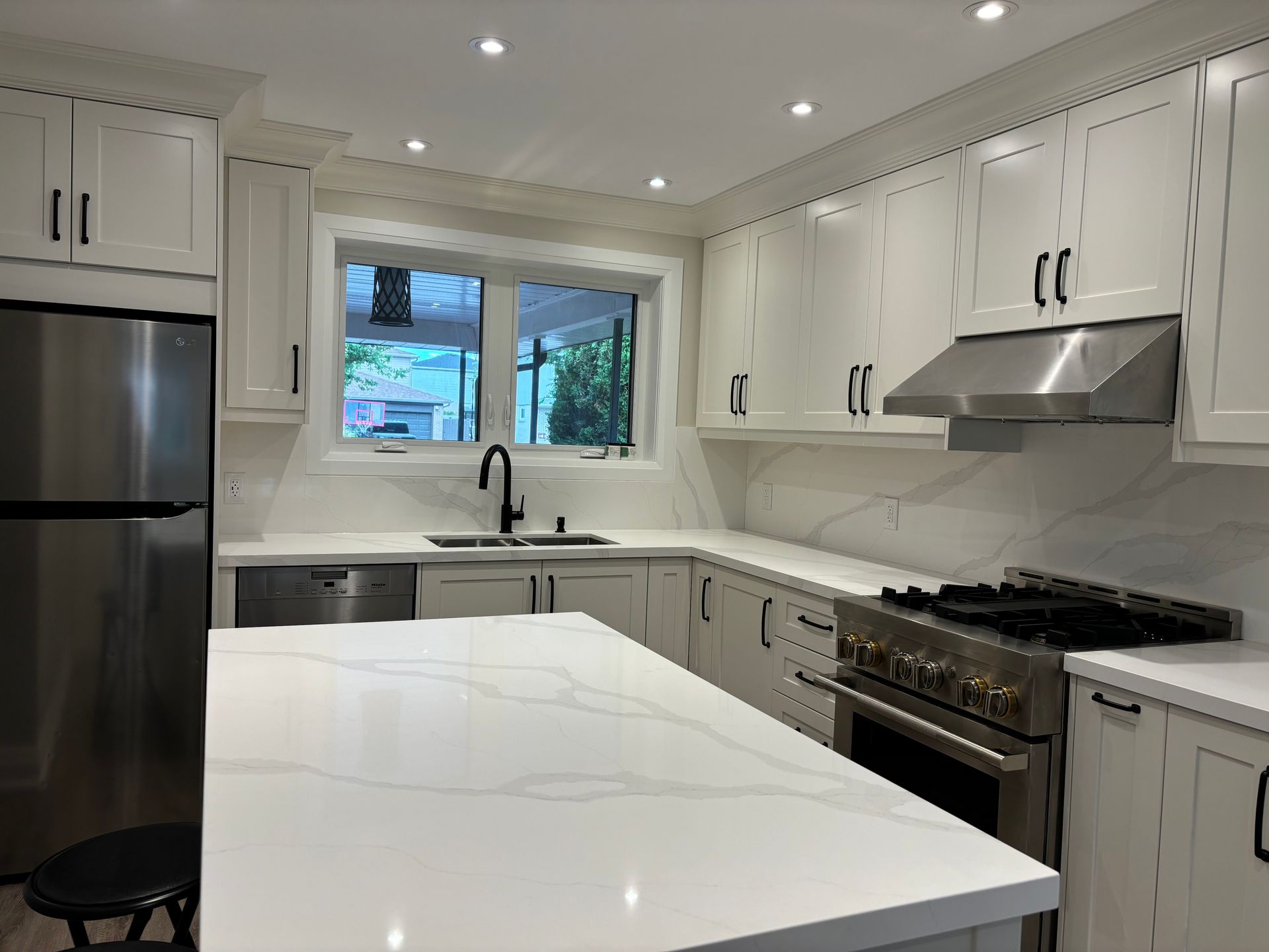 White kitchen with quartz countertops, stainless steel appliances, and black hardware.