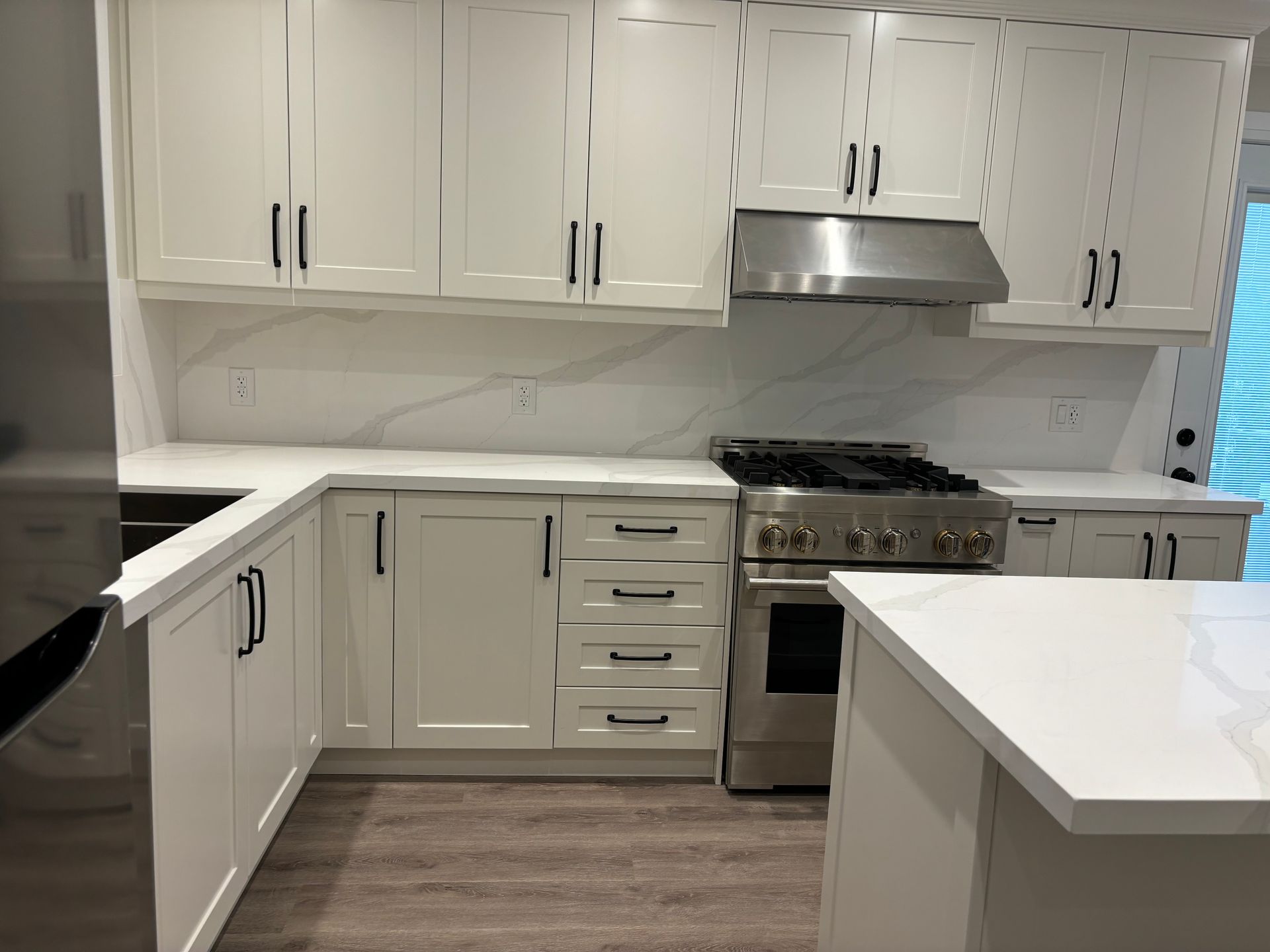 White kitchen with cabinets, countertops, stainless steel appliances, and a cooktop.