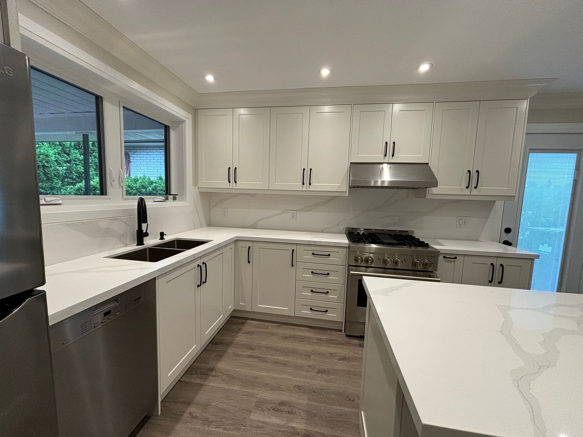 Modern white kitchen with stainless steel appliances, marble backsplash, and island.