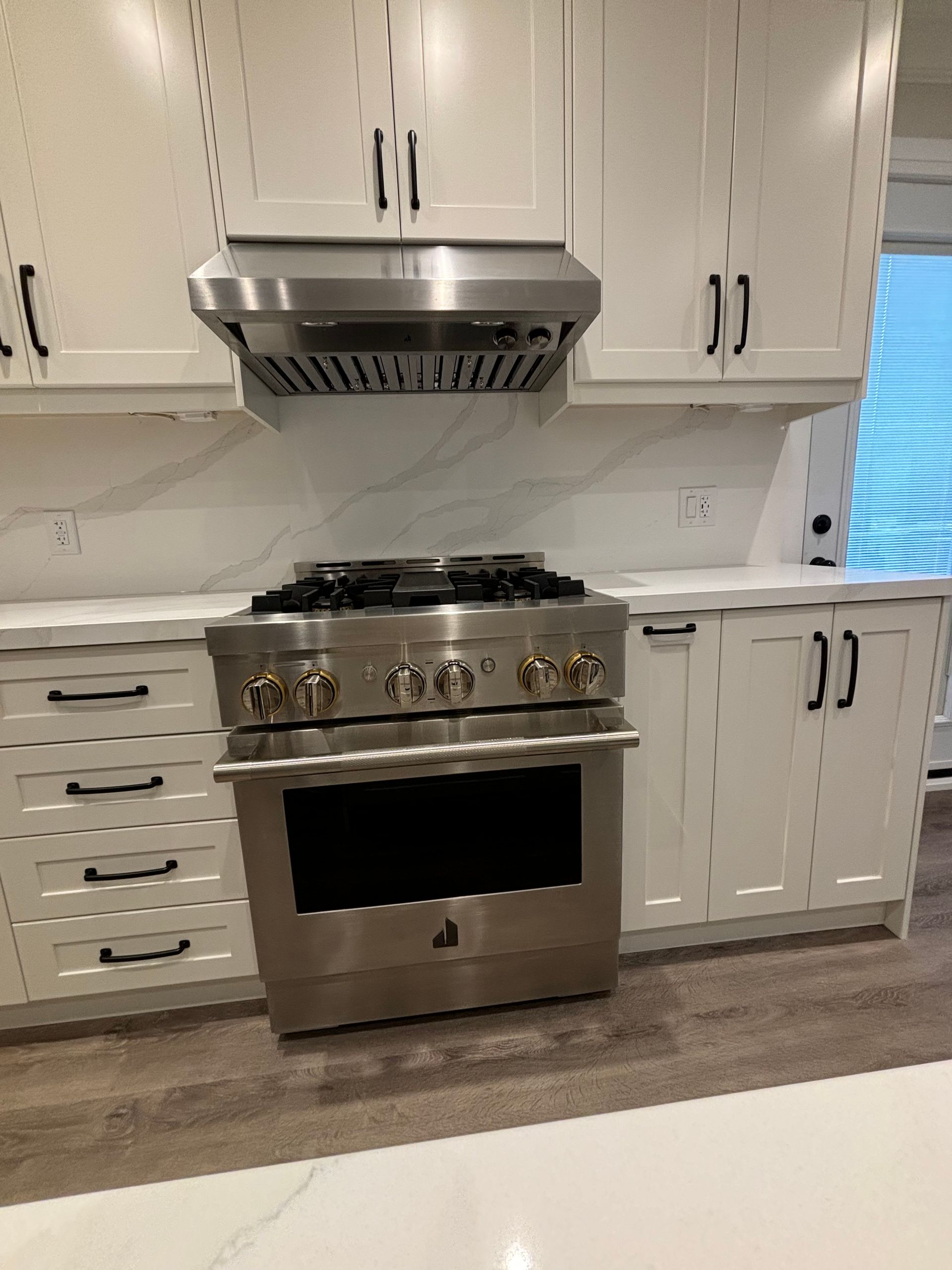 Stainless steel oven and range hood in a white kitchen with cabinets.