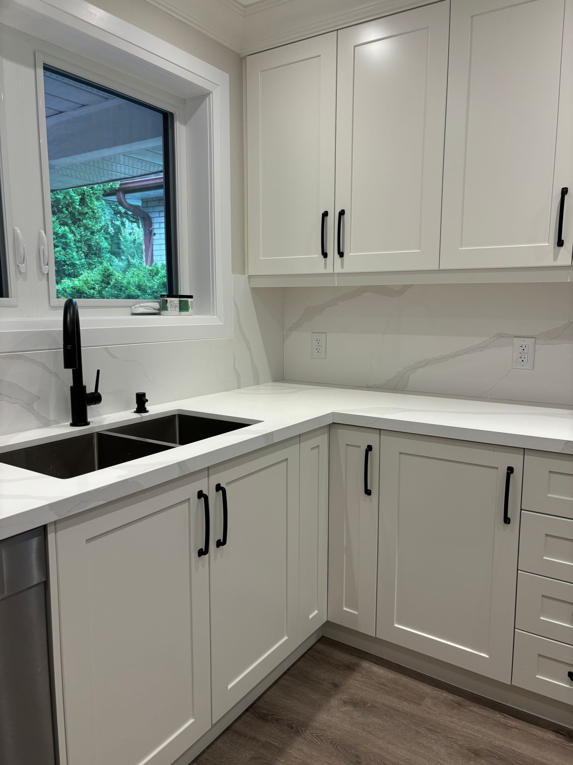 White kitchen with black accents. Sink, cabinets, window with greenery view.