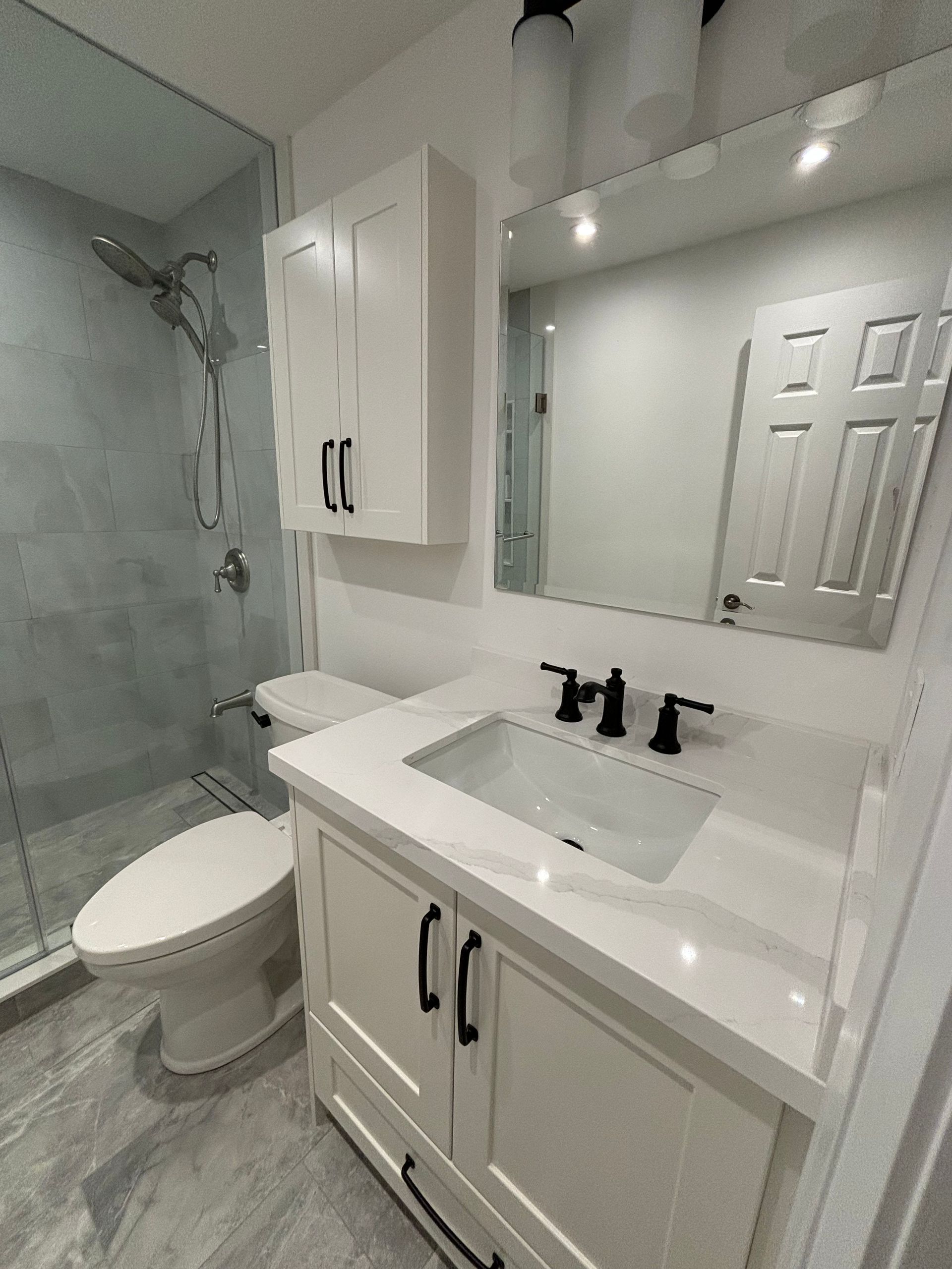 Modern white bathroom with shower, toilet, vanity, and cabinet. Gray and white color scheme.