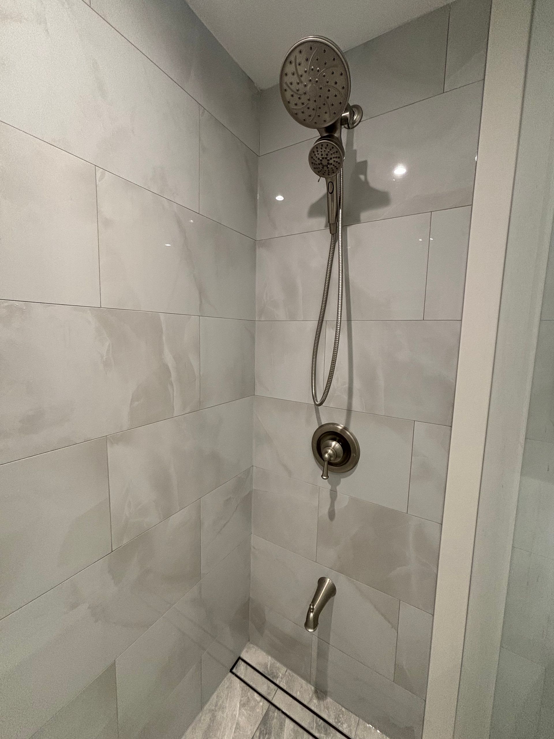 Shower stall with gray tile, showerhead, and faucet.