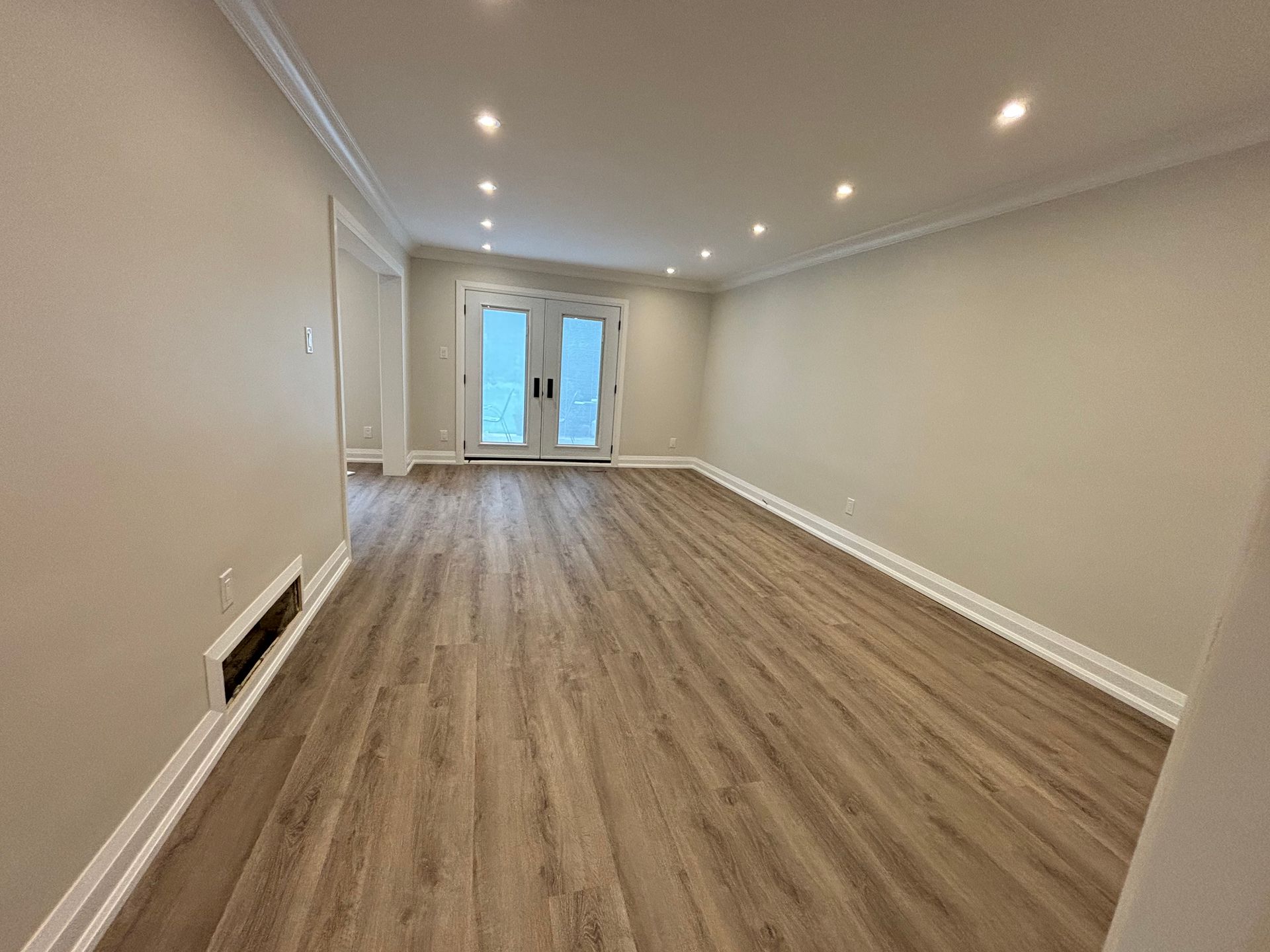 Empty room with light wood floors, beige walls, and French doors.