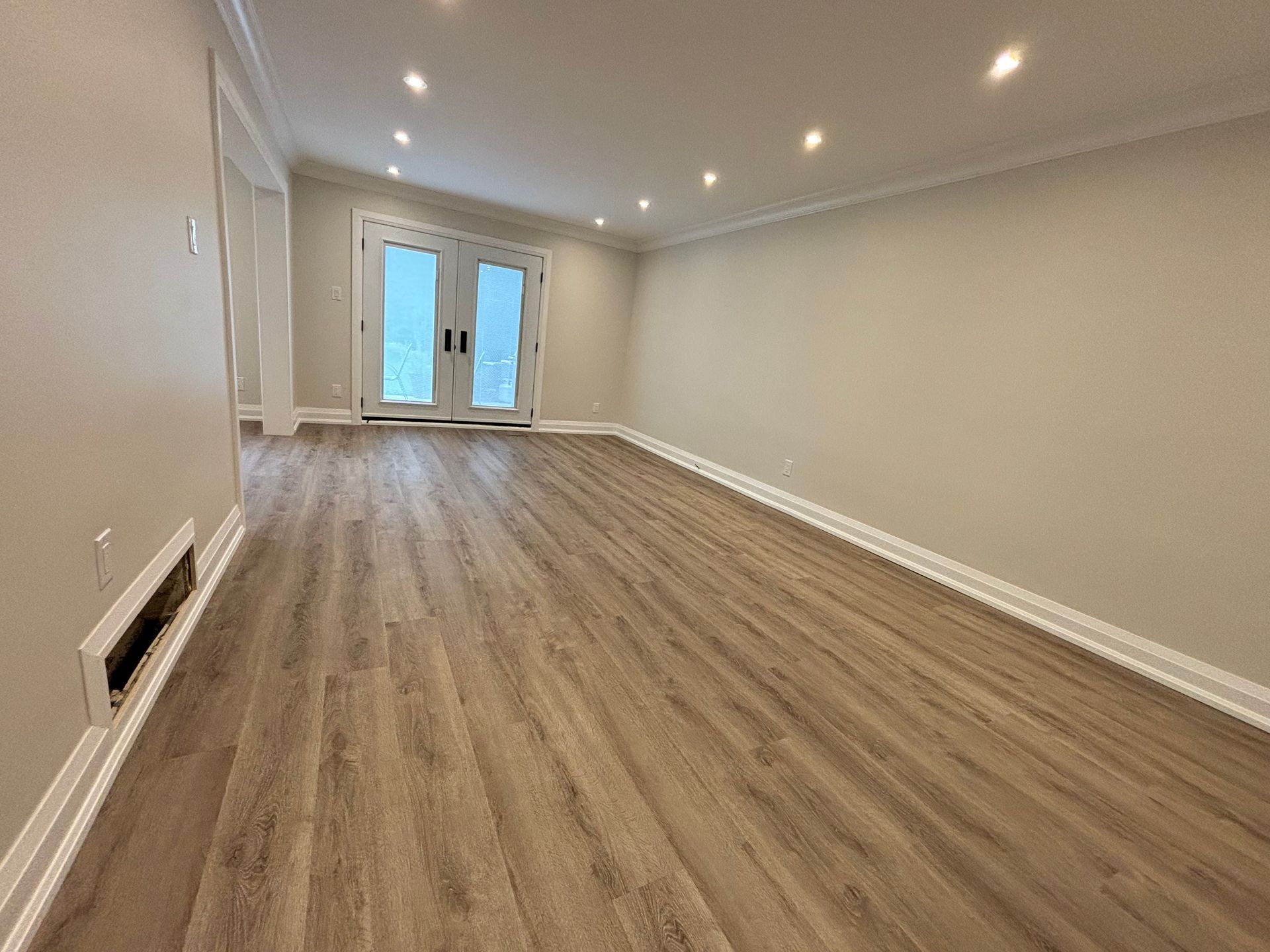 Empty room with wood-look flooring, beige walls, white trim, and recessed lighting. French doors at the back.