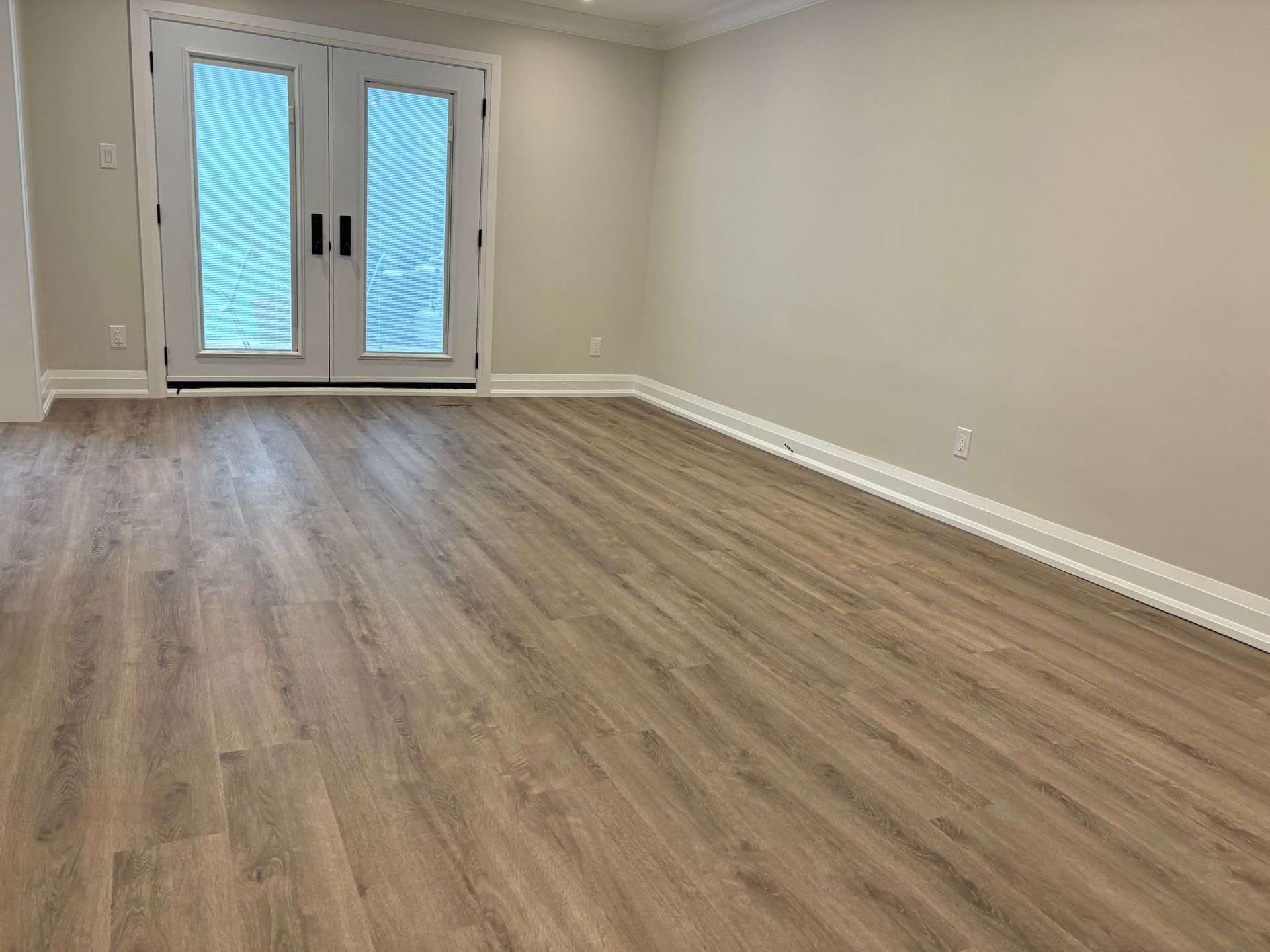 Empty room with light wood-look flooring, beige walls, white trim, and French doors.