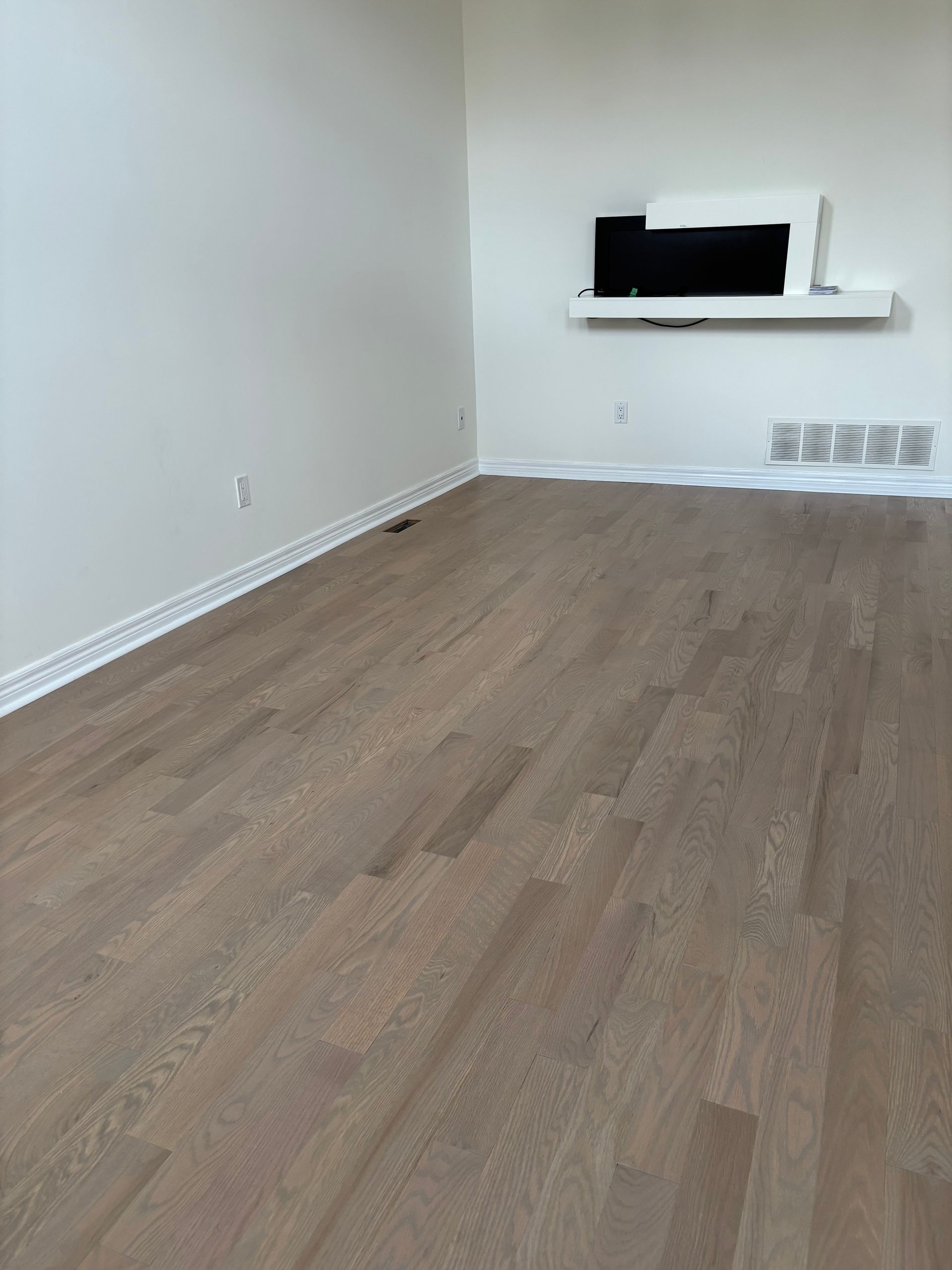 Empty room with wood floors and a mounted TV on a white shelf. White walls.