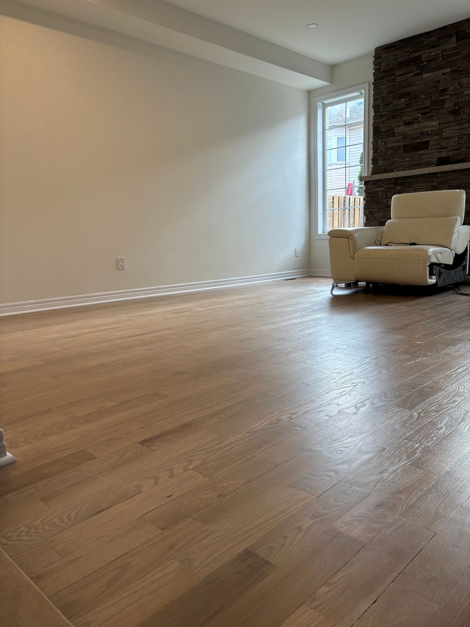 Empty room with light wood floors, white walls, a window, and a beige recliner chair.