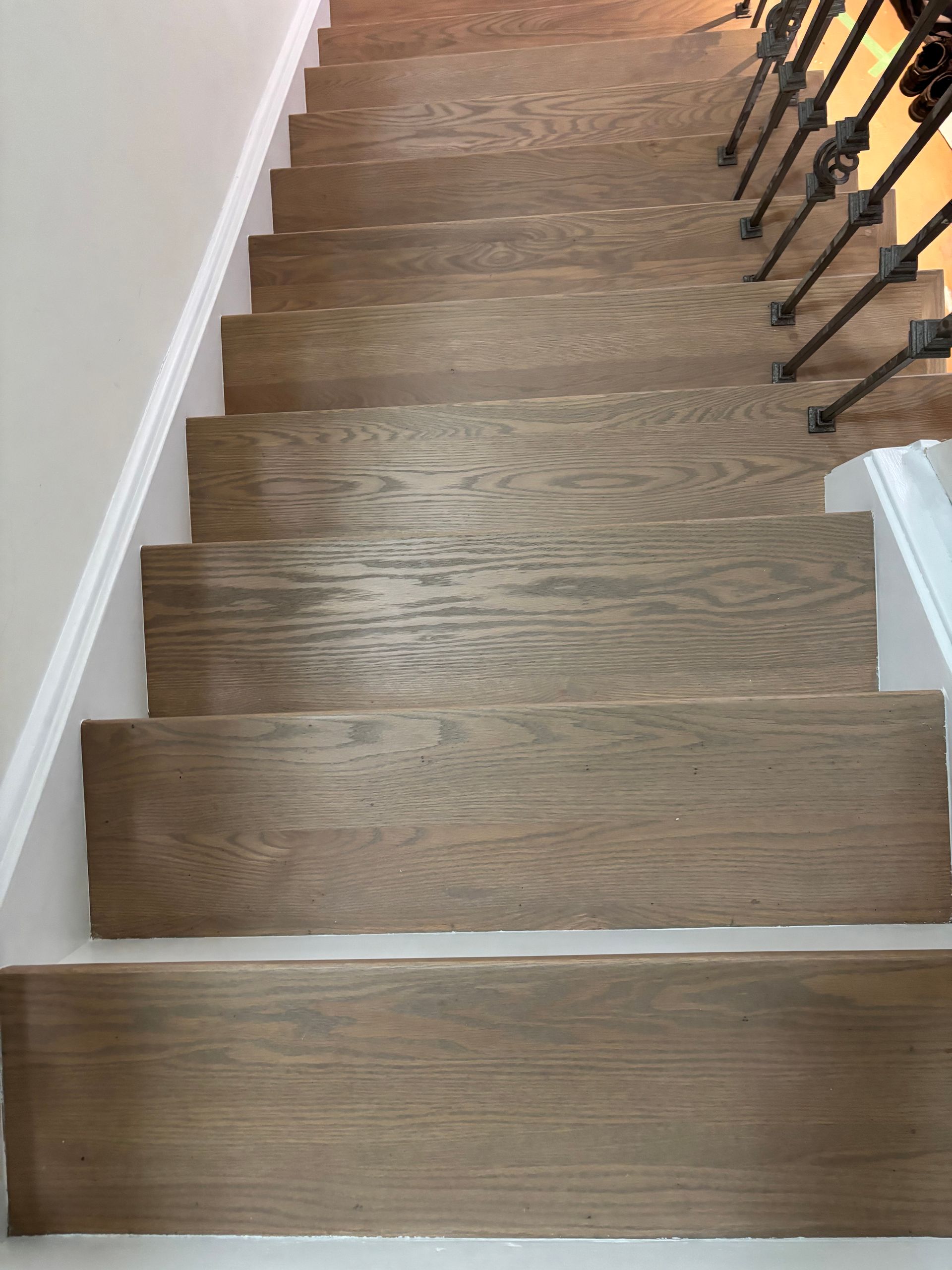Wooden staircase with a white painted wall on one side, black wrought iron railing on the other.