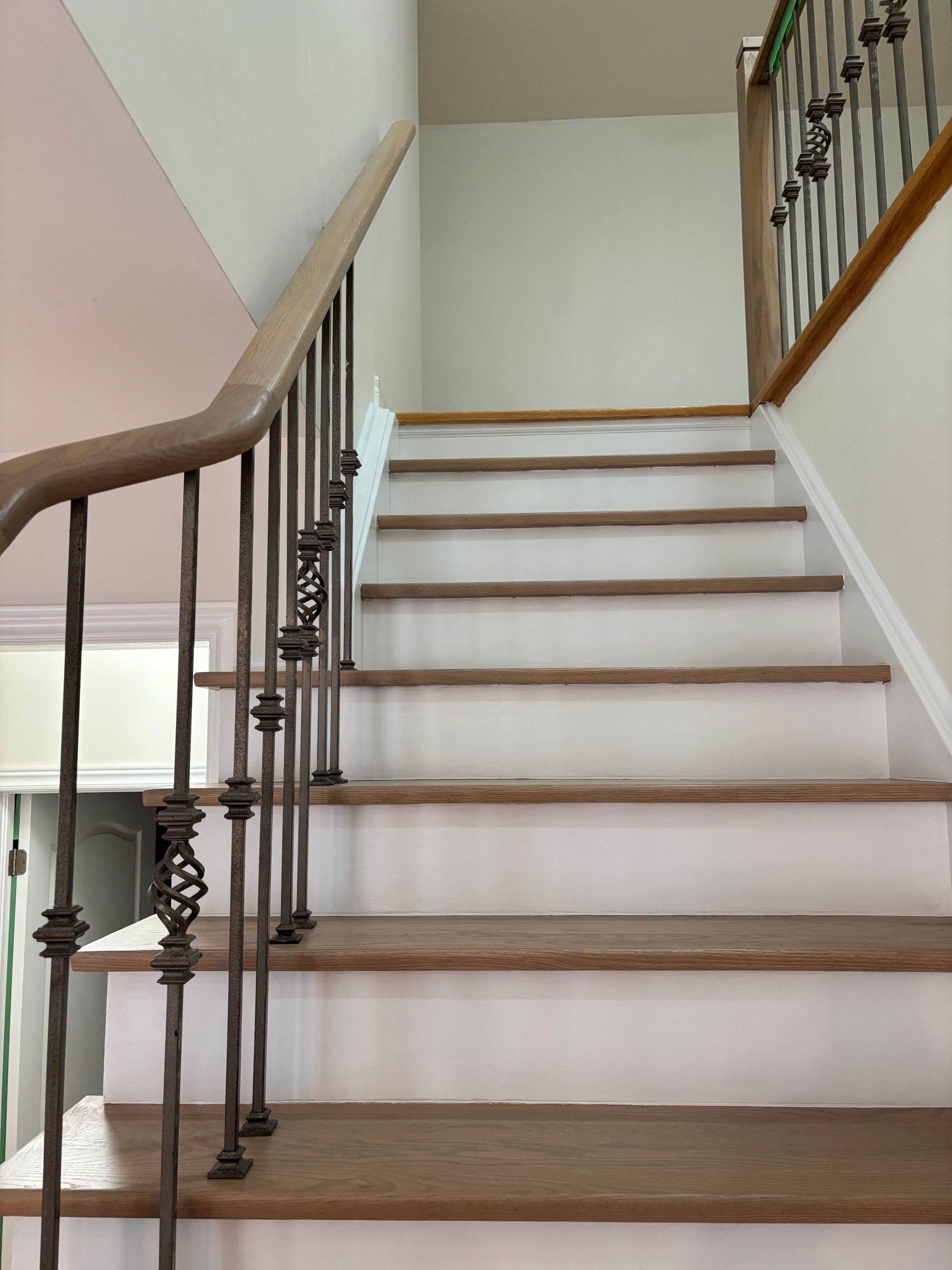 Wooden staircase with white risers and wrought iron railing.