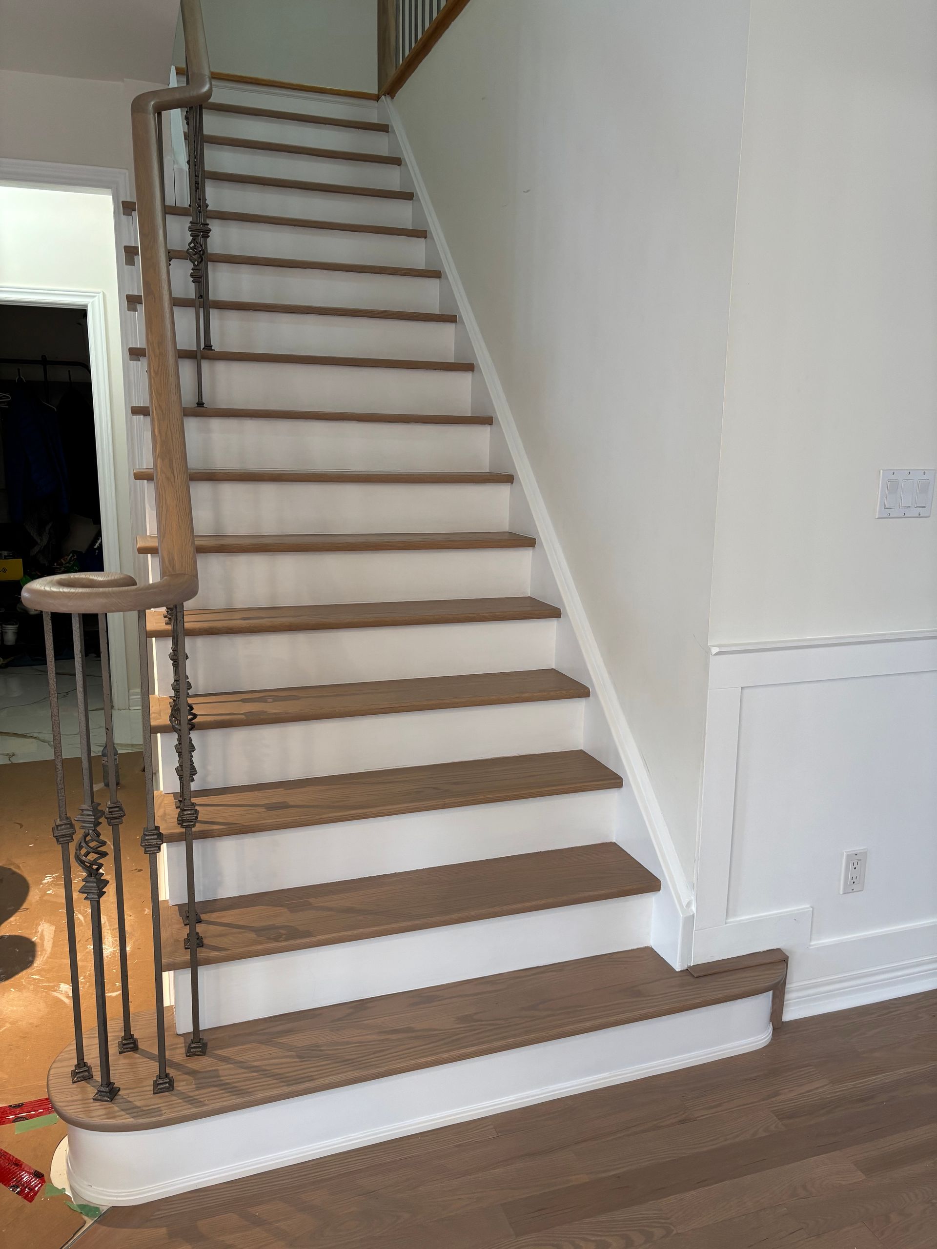 Wooden staircase with white risers, dark treads, and ornate wrought-iron railing.