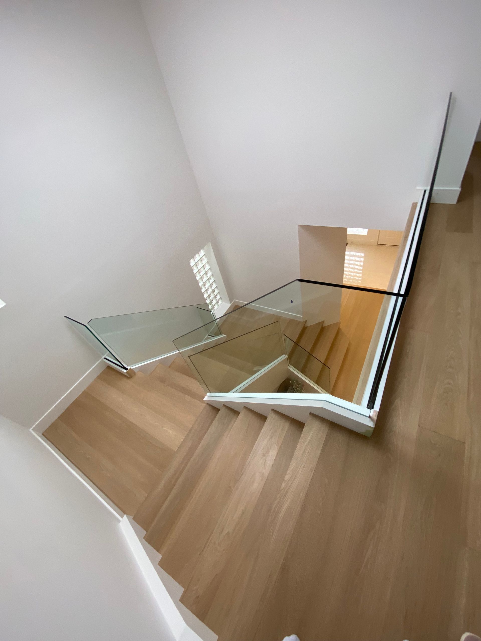 Wooden staircase with glass railing. Light wood steps, white walls. Top-down view.