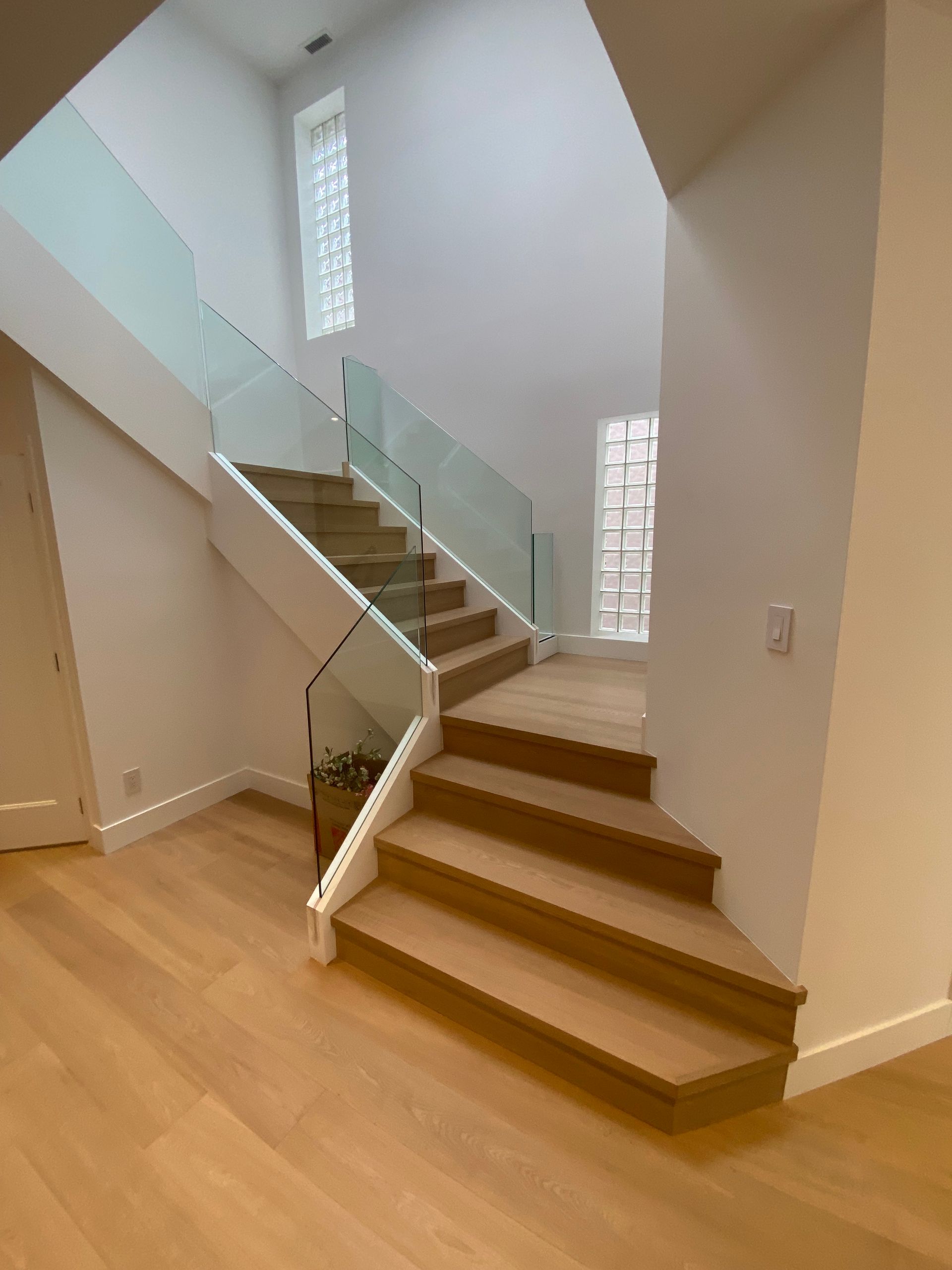 Modern staircase with glass railing and wooden steps.