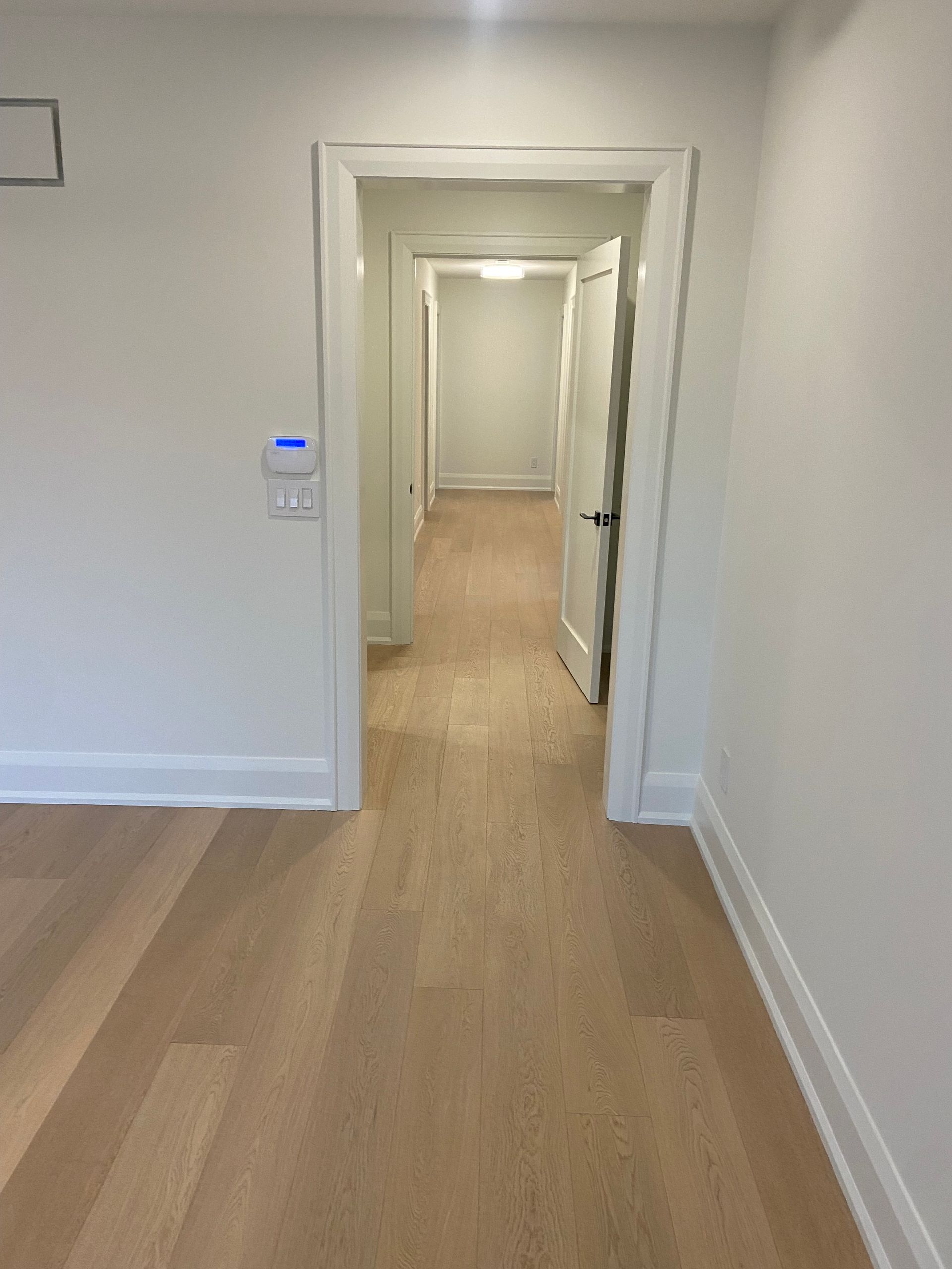 Hallway with light wood floors, white walls, and open doors.