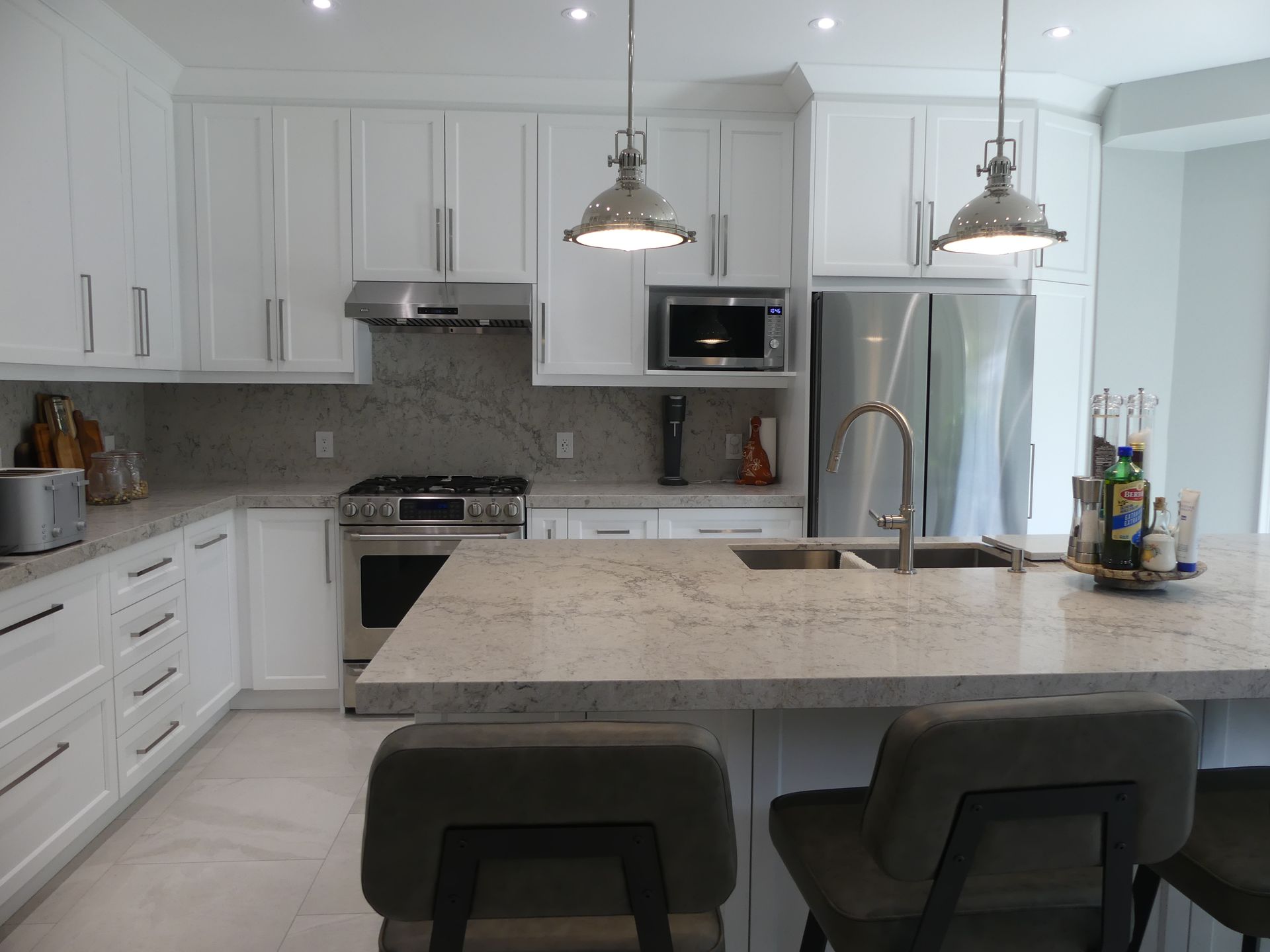 White kitchen with island, stainless appliances, and pendant lights.