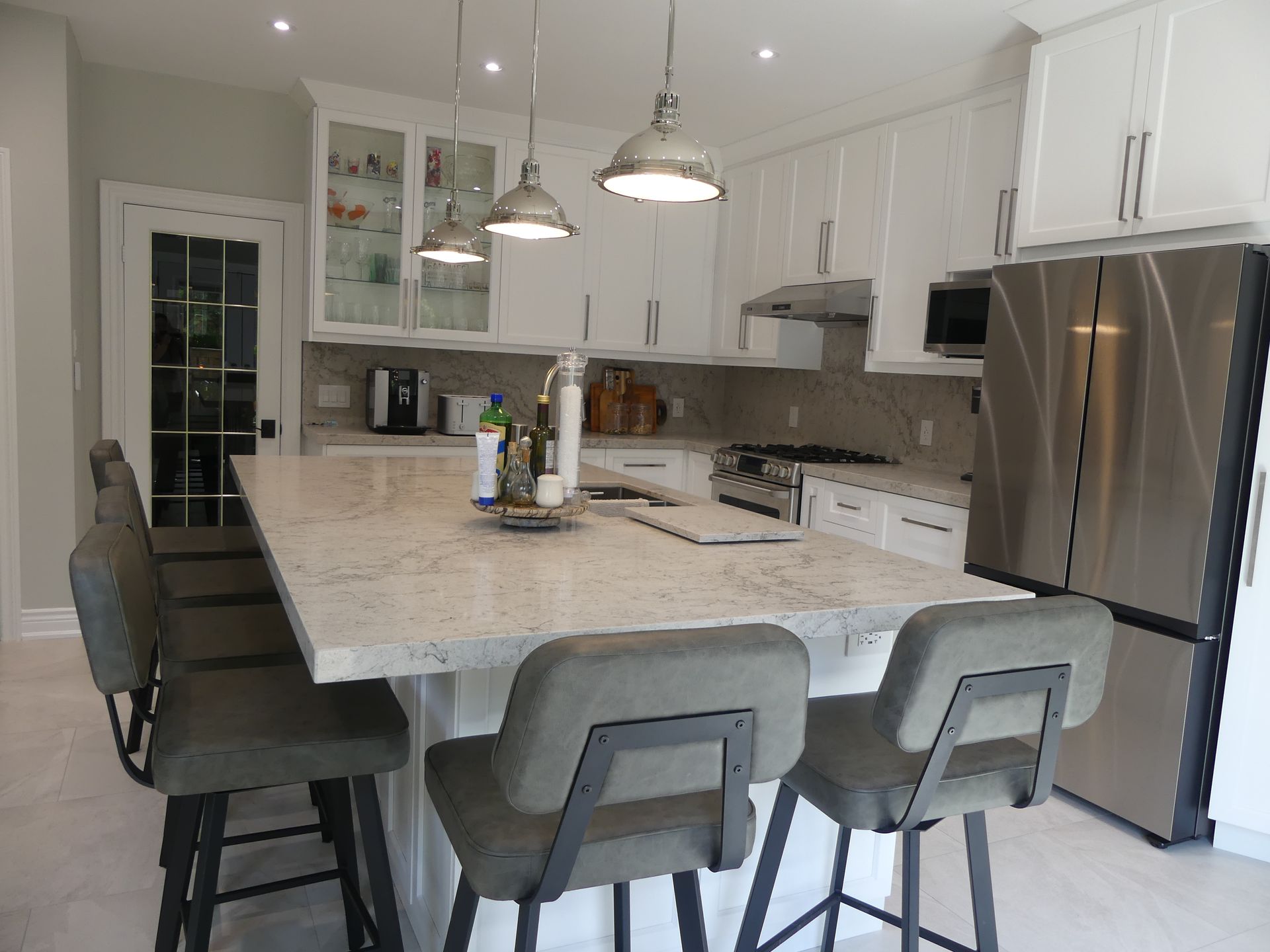 Modern white kitchen with island seating, stainless steel appliances, and pendant lights.