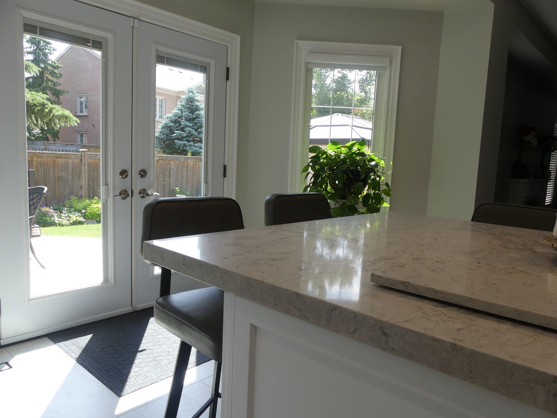 Kitchen with counter, two stools, French doors, and a window overlooking a backyard.