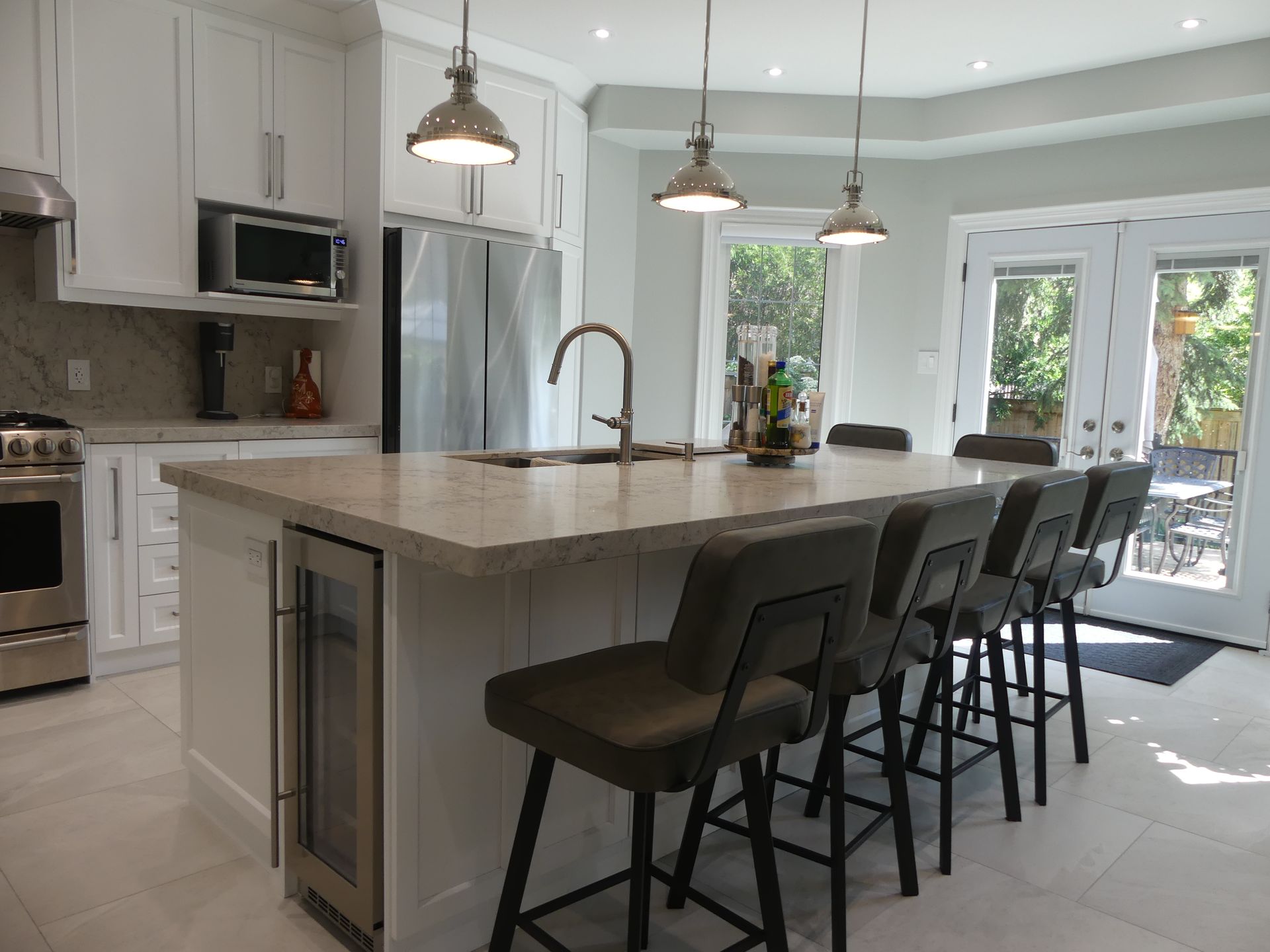 Modern white kitchen with island, seating, and stainless steel appliances.