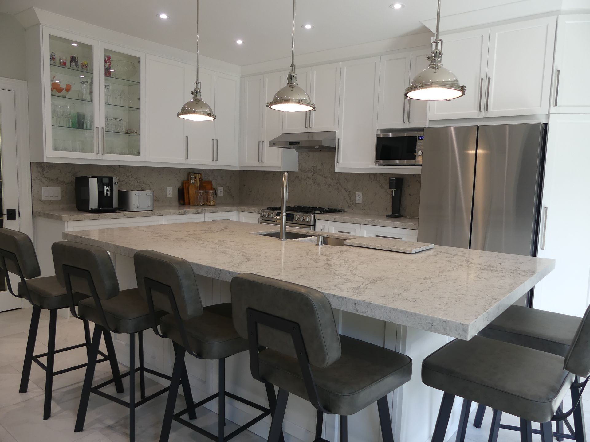 Modern white kitchen with a granite island, stainless steel appliances, and bar stools.