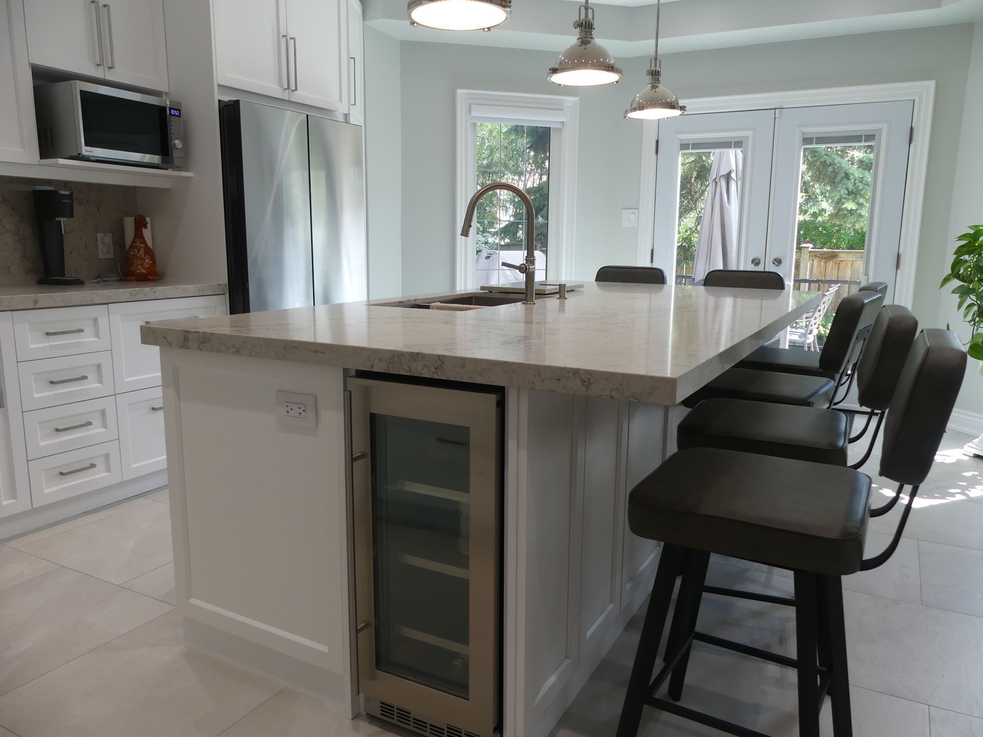 Modern white kitchen with island, seating, wine fridge, stainless steel appliances, and outdoor access.