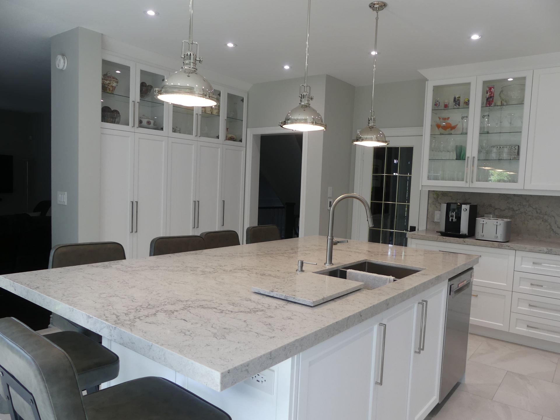 Modern white kitchen with island, pendant lights, and stainless steel appliances.