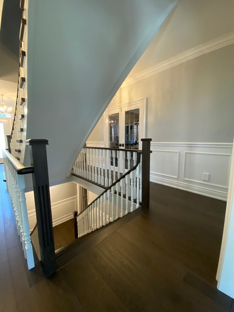 Dark wood flooring, staircase with white and black balustrade, gray walls, and white molding.