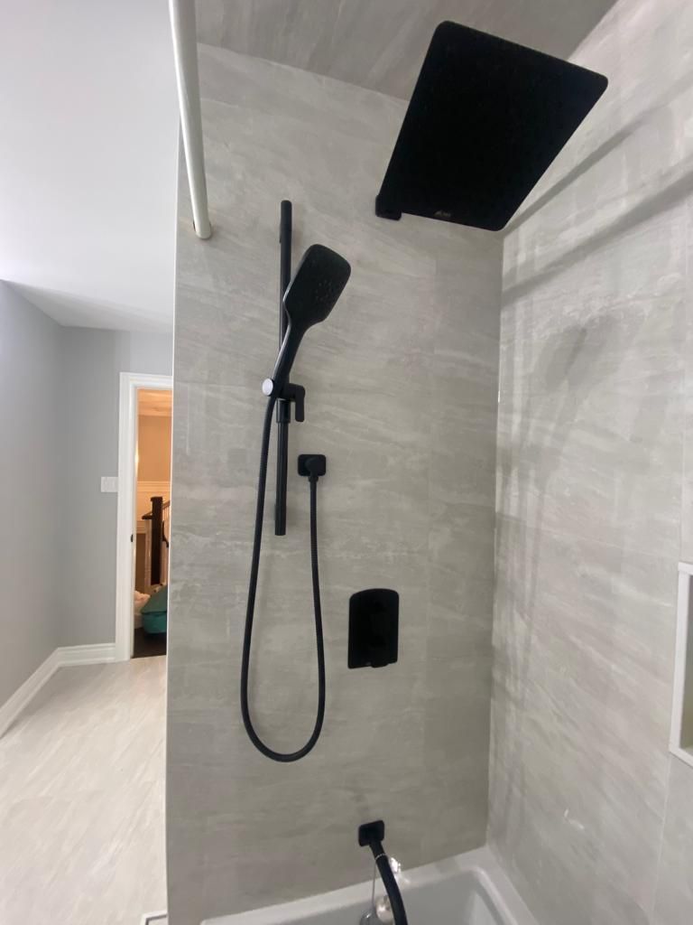 Black shower fixtures on gray tiled wall, with hand shower and overhead showerhead.