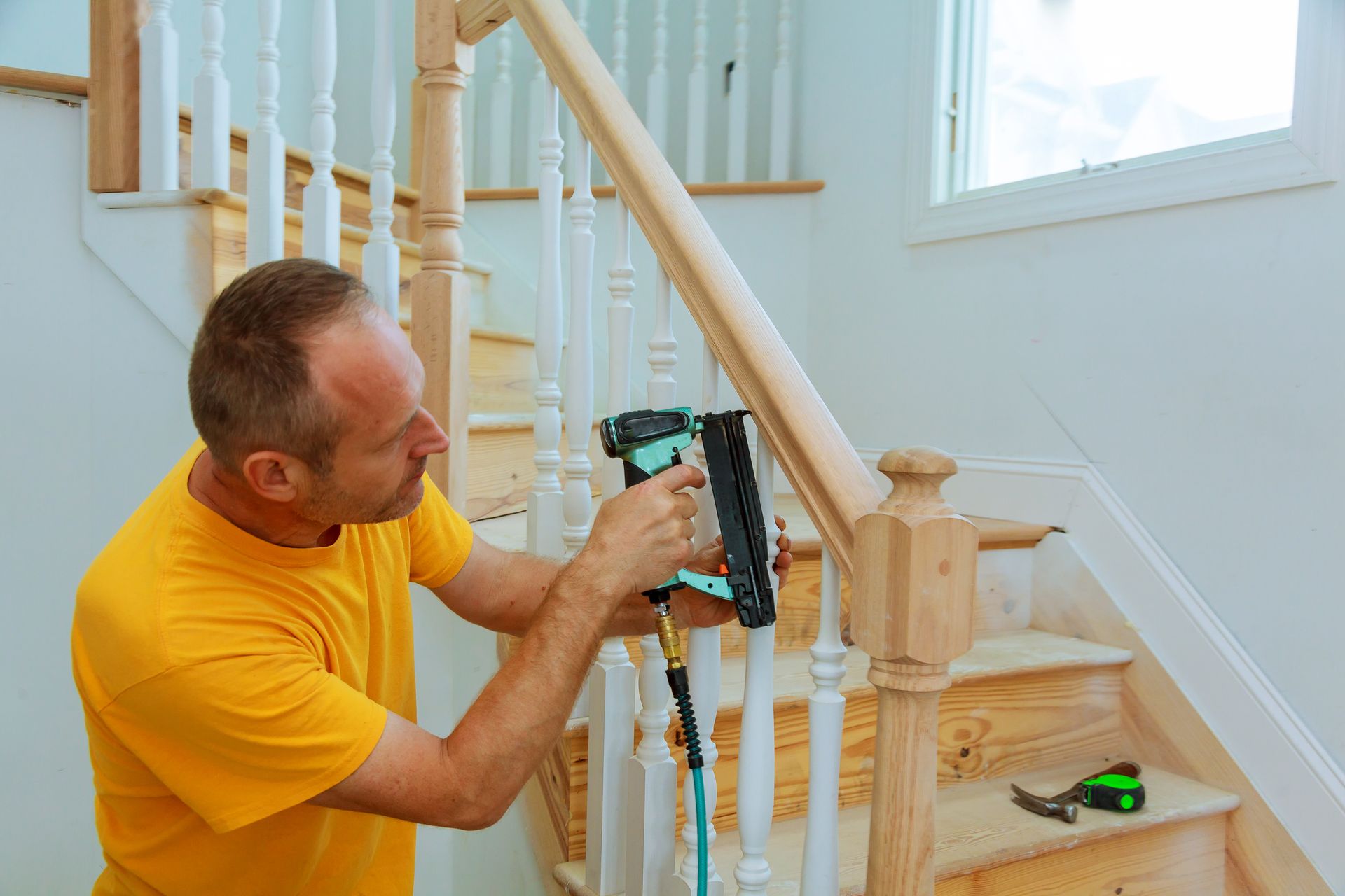 A man is installing a wooden railing on a set of stairs.