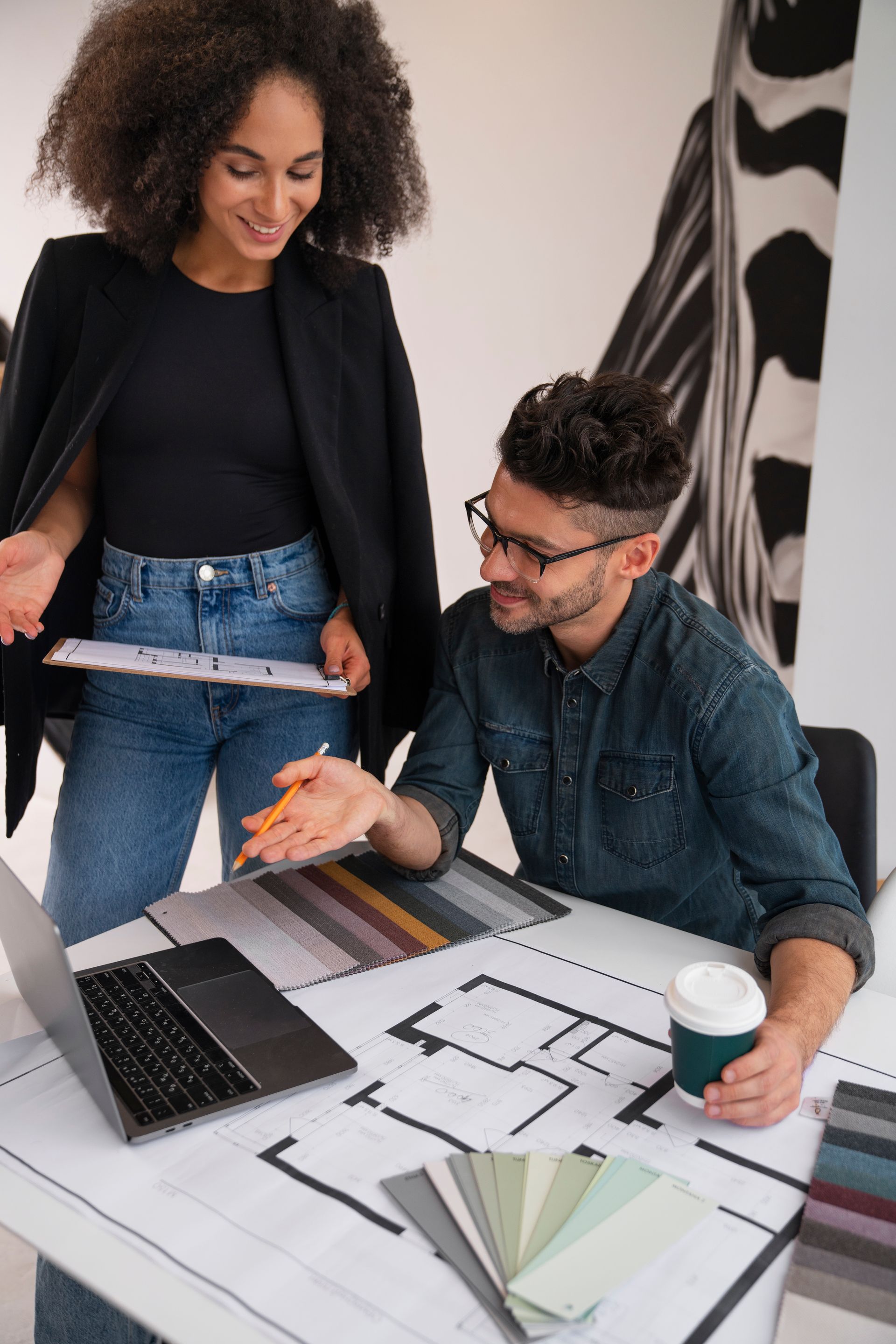 A man and a woman are sitting at a table looking at a laptop.