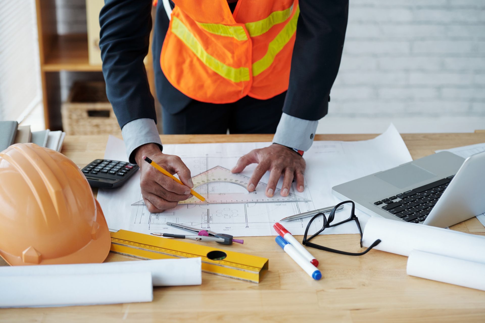 A construction worker is standing at a desk drawing a blueprint.