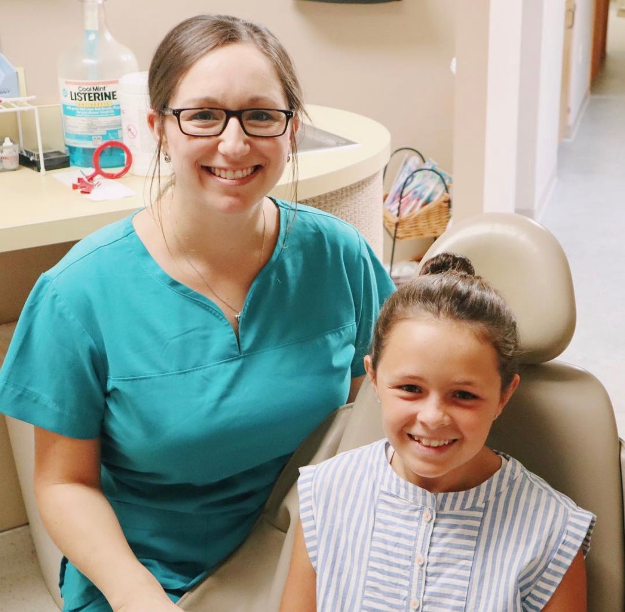 A hygienist is sitting next to a little girl in a dental chair