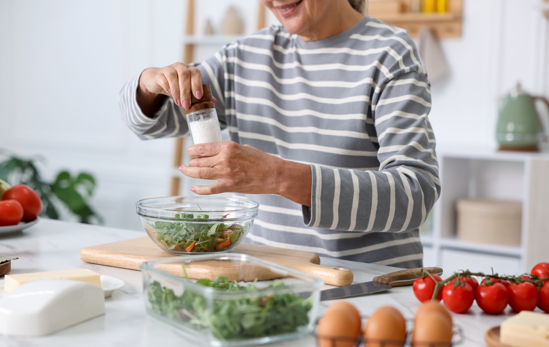 Person adding salt to salad in kitchen.