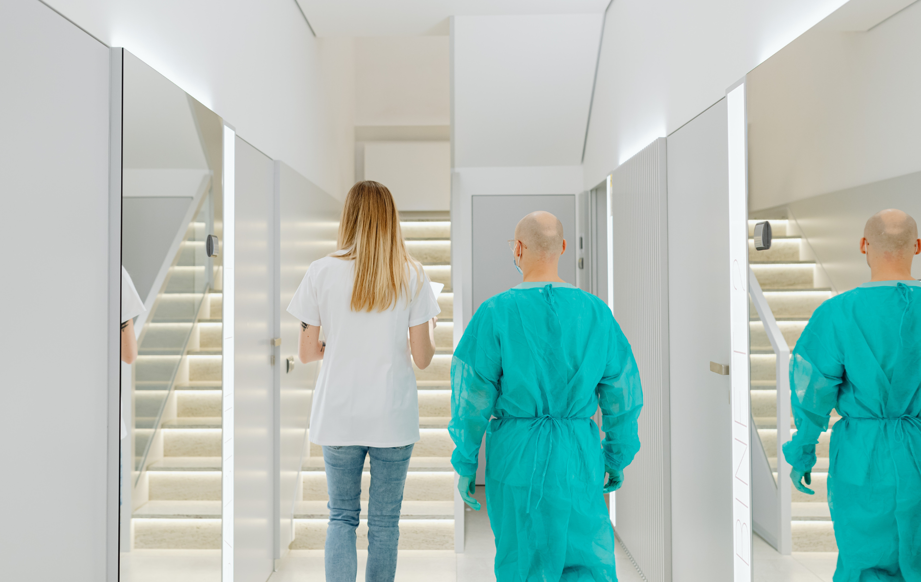 A medical hallway with three people walking: a person in scrubs, a person in a white top and jeans