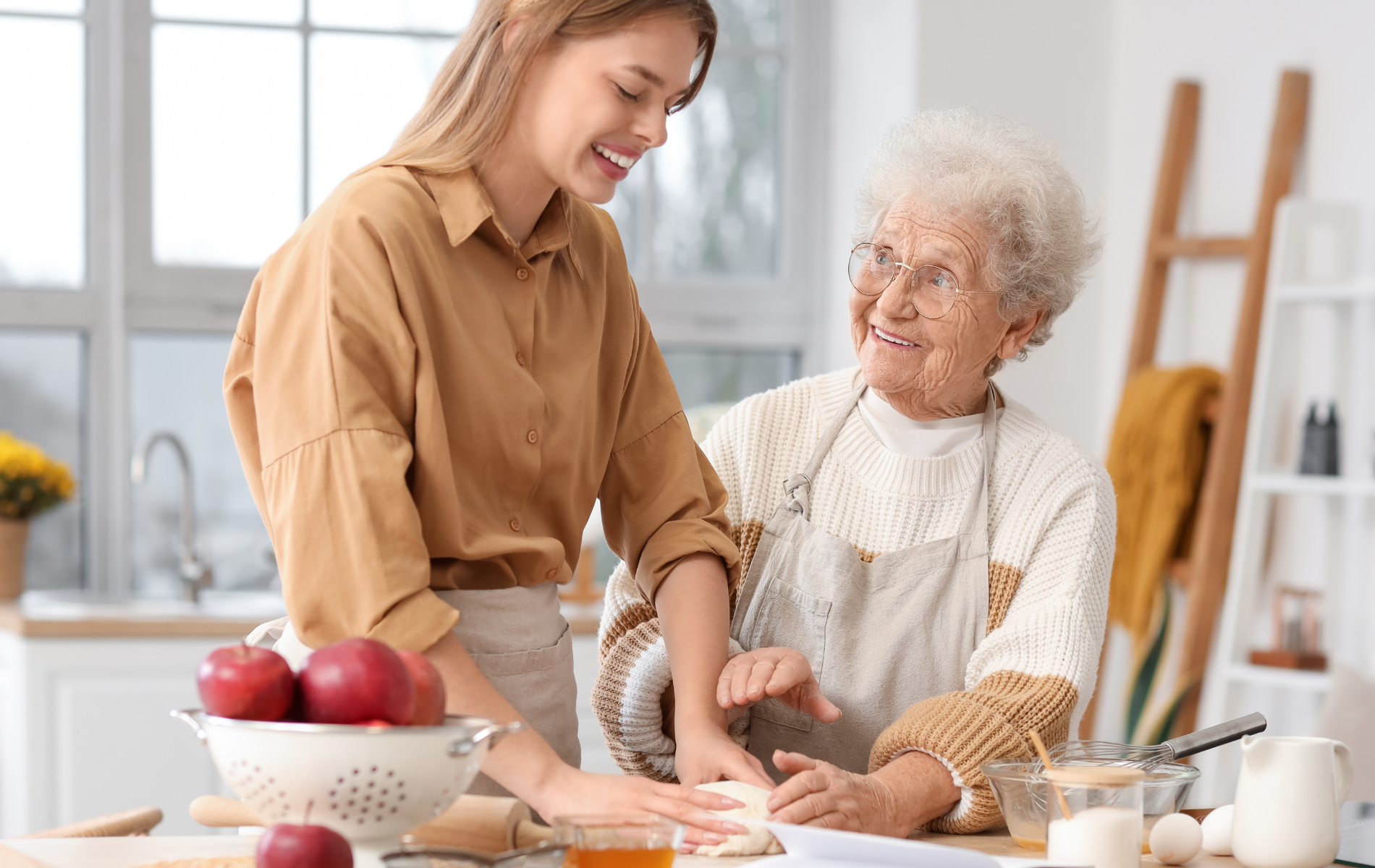 Young woman and elderly woman smiling, kneading dough in a kitchen.