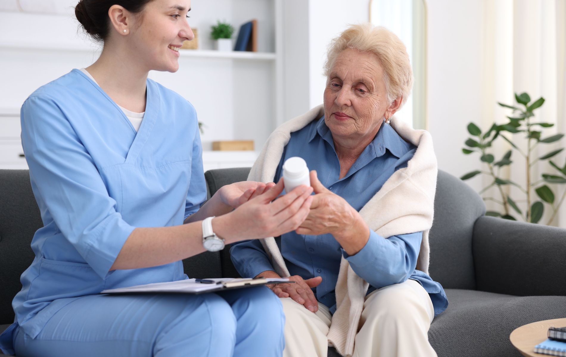 Caregiver assisting a senior woman with a cane sitting on a sofa.