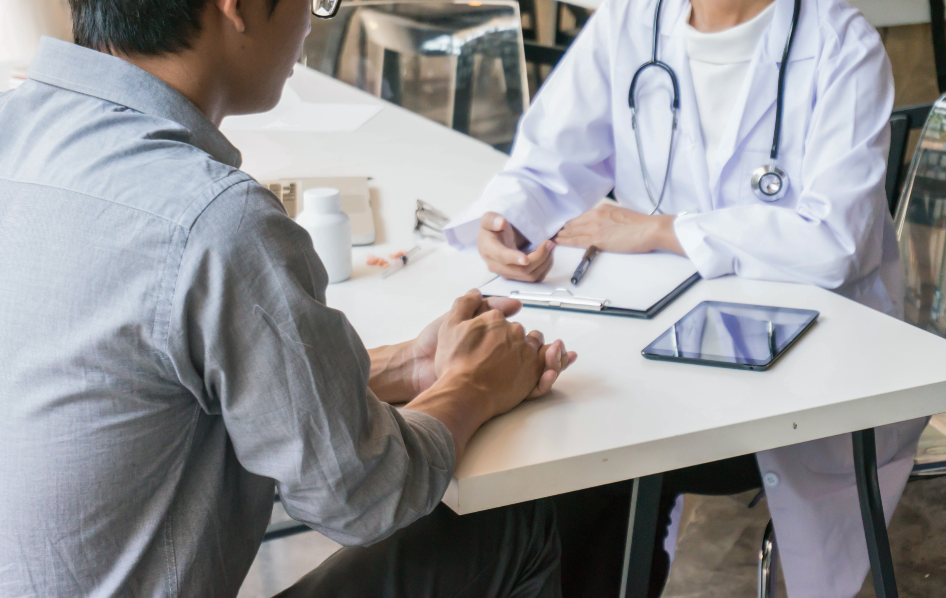 A patient consults with a doctor in an office setting. The doctor writes on a clipboard.