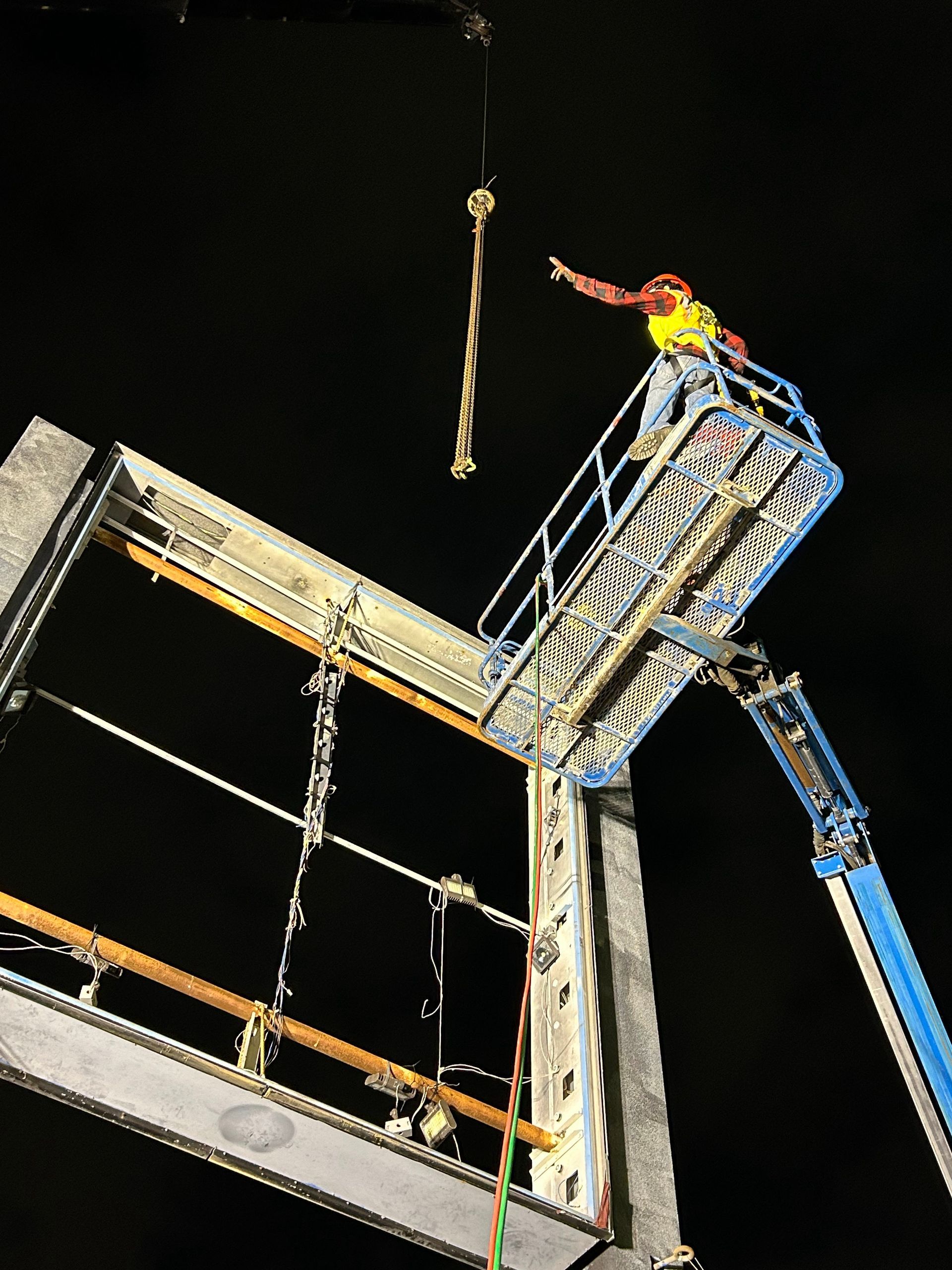 A man is standing on top of a crane at night.