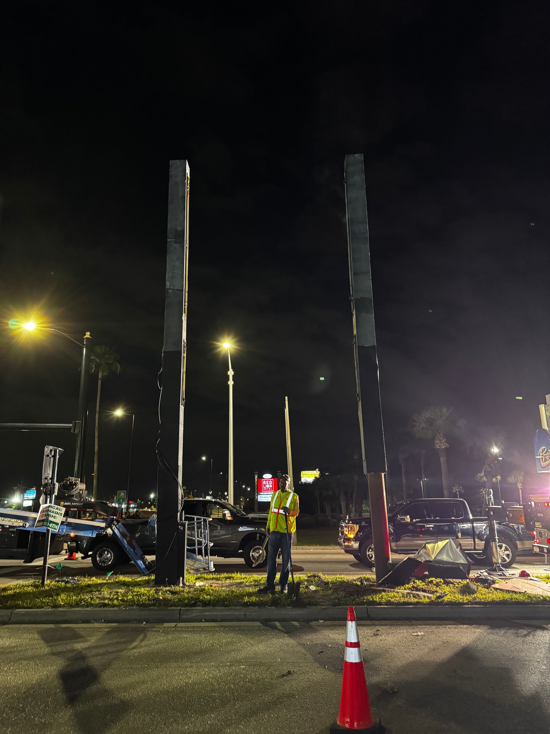 A man in a yellow vest is standing in a parking lot at night