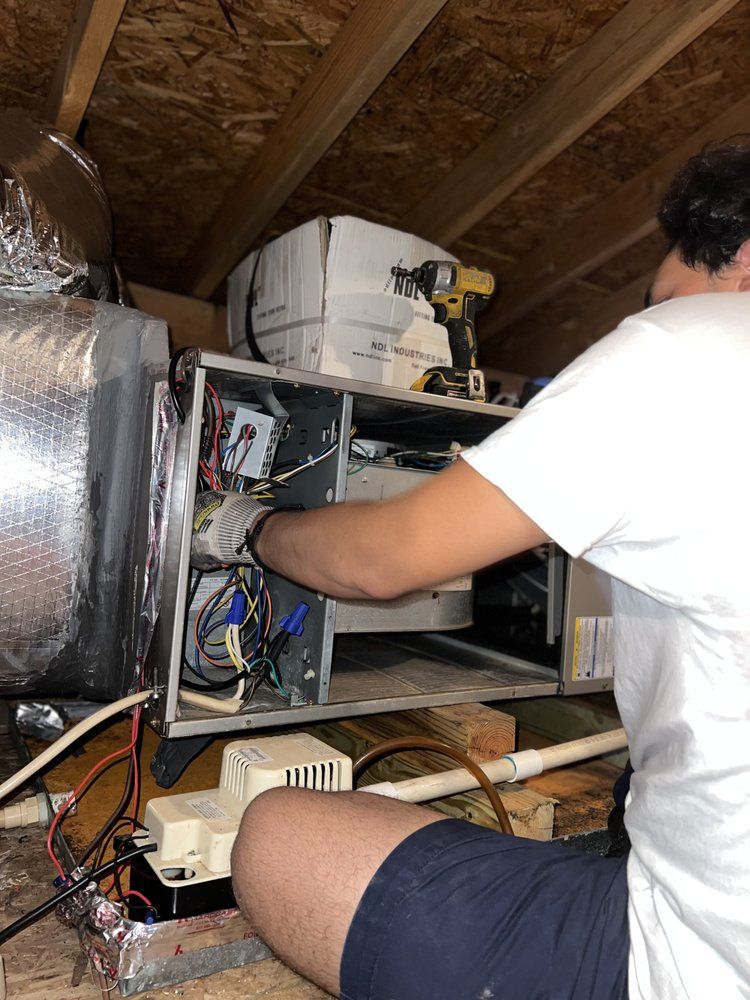 A man is working on an air conditioner in an attic.