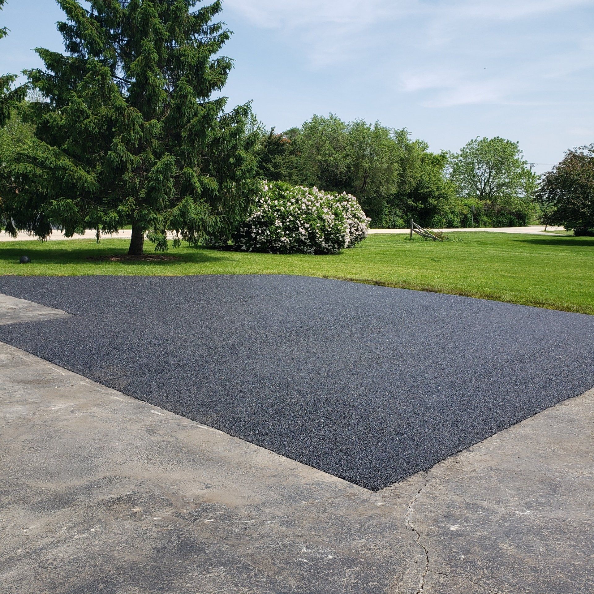 Black rubber surfacing on asphalt near green grass and trees.