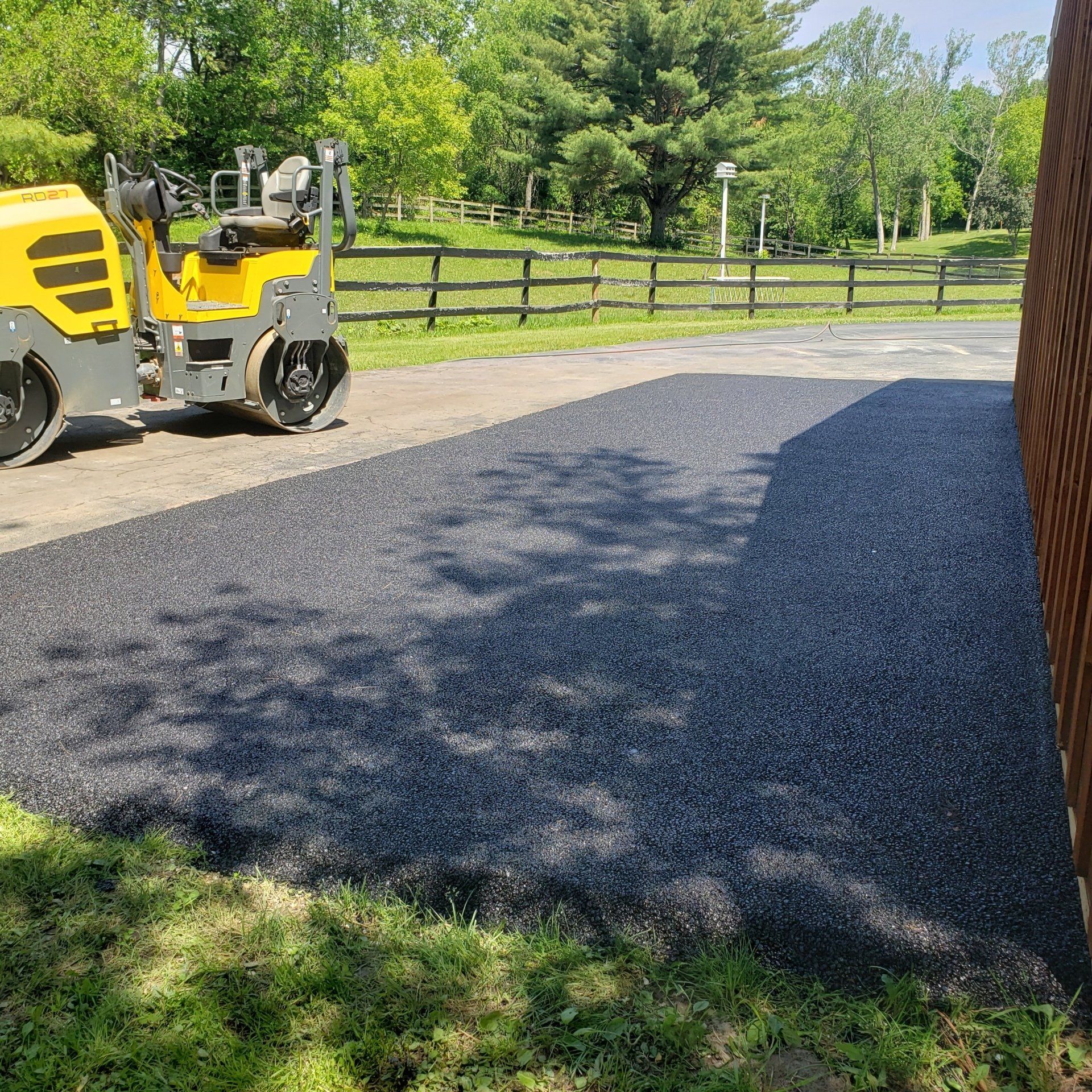 Asphalt paving in progress; a yellow roller compacting fresh black asphalt.