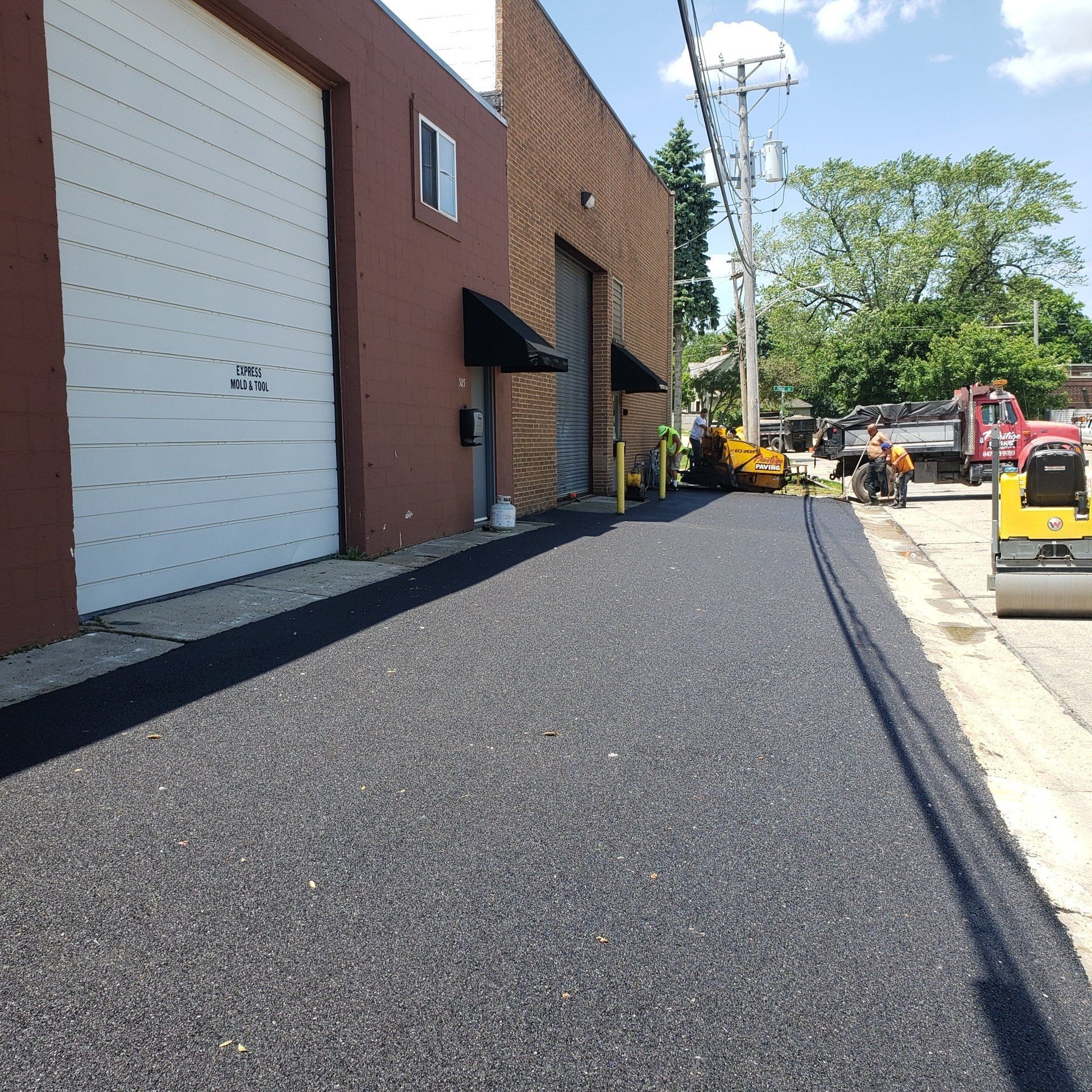 Freshly paved asphalt driveway next to a brick building with a white garage door.