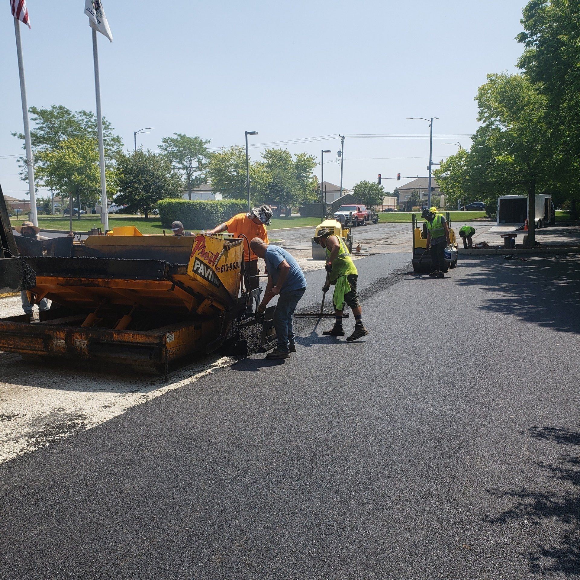 Workers paving a road with asphalt; sunny day, asphalt machine, workers in safety vests.