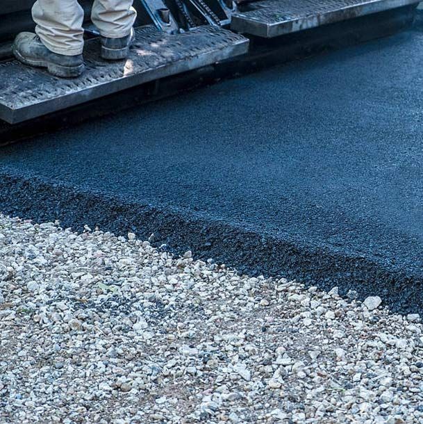 Asphalt paving machine rolls on top of black asphalt, with two people on top.