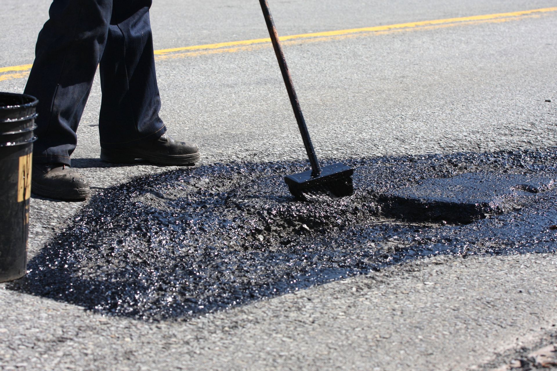 A road construction worker spreads tar in a pothole. A road construction worker spreads tar in a pothole.