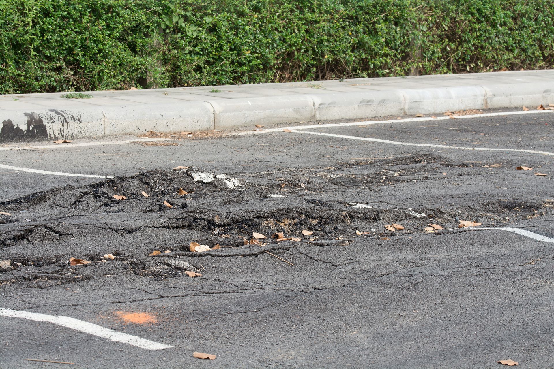 Cracked parking lot with several visible potholes requiring services from a paving contractor.