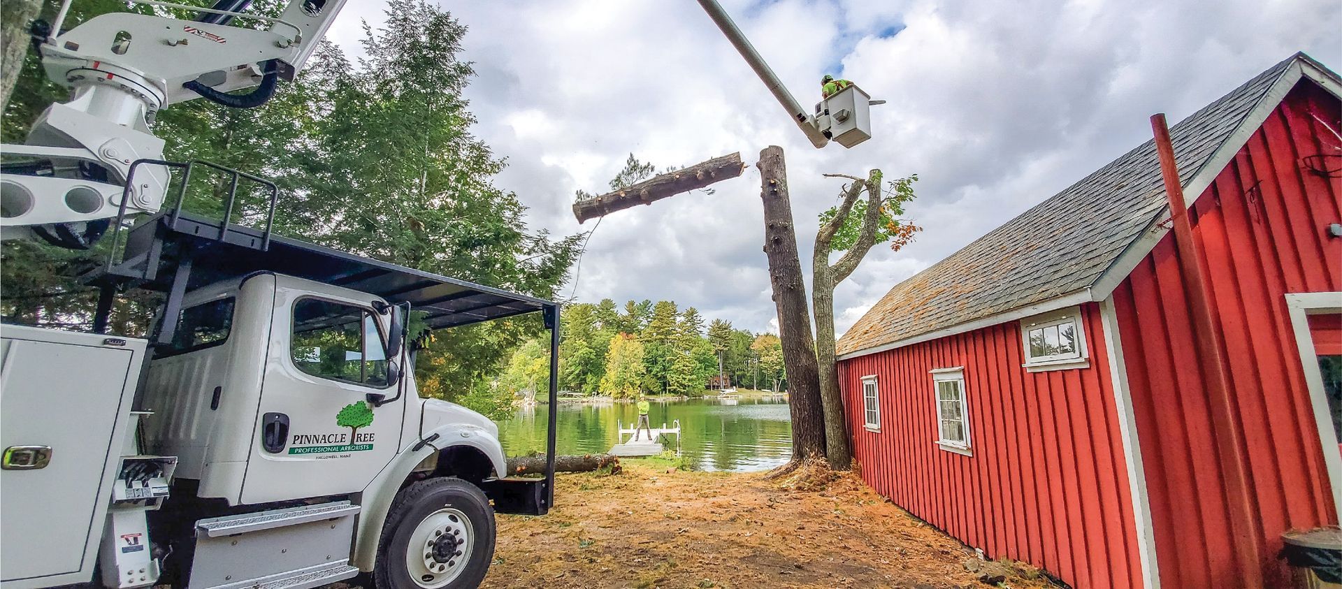 A white truck is cutting a tree in front of a red barn.